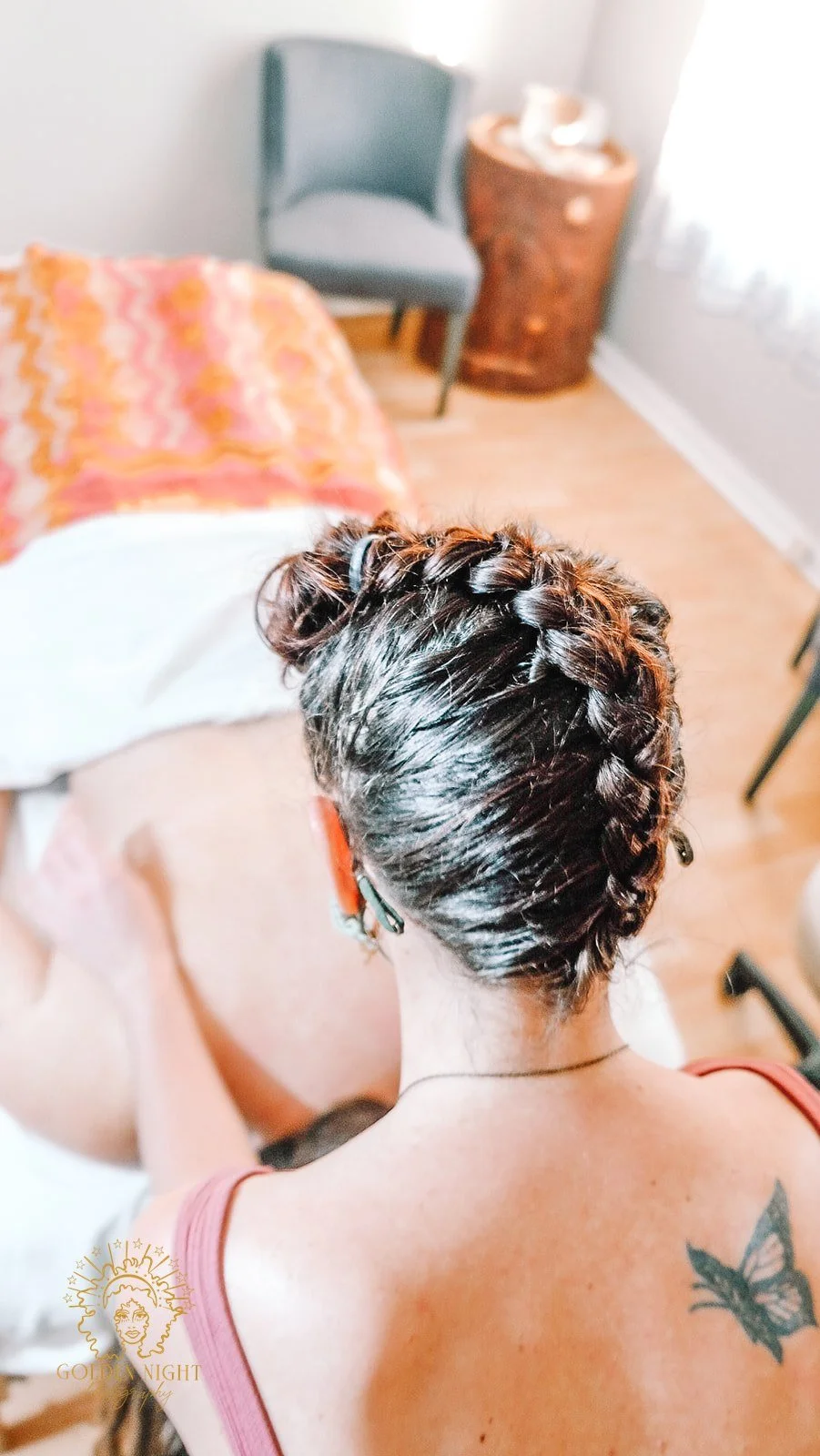 a white person with a long french braid is facing away from the camera with their hands on the back of a white person on a massage table