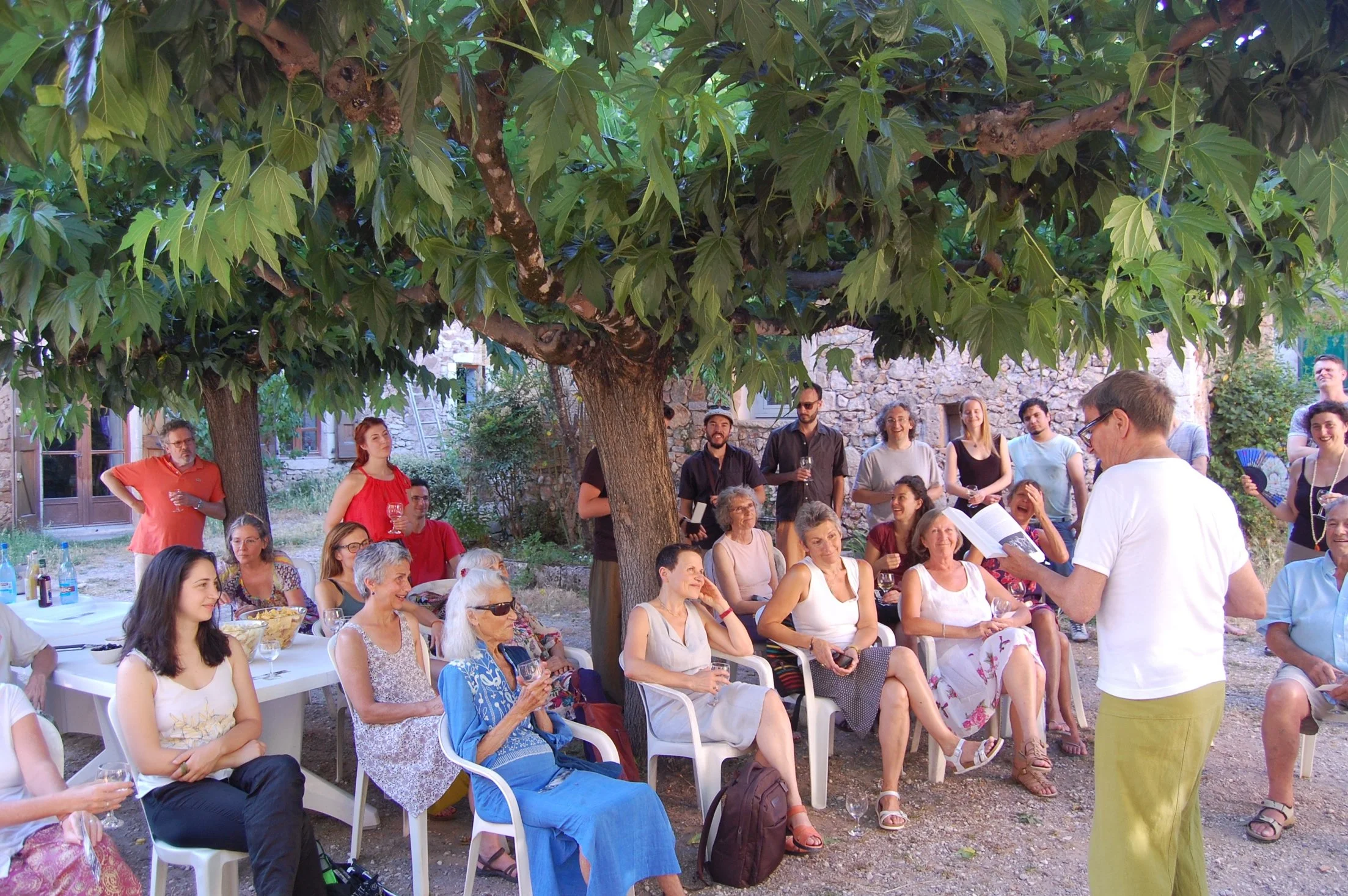 Ian Magilton reads from his book to a gathering of people beneath the mulberry trees in the courtyard at Malérargues.