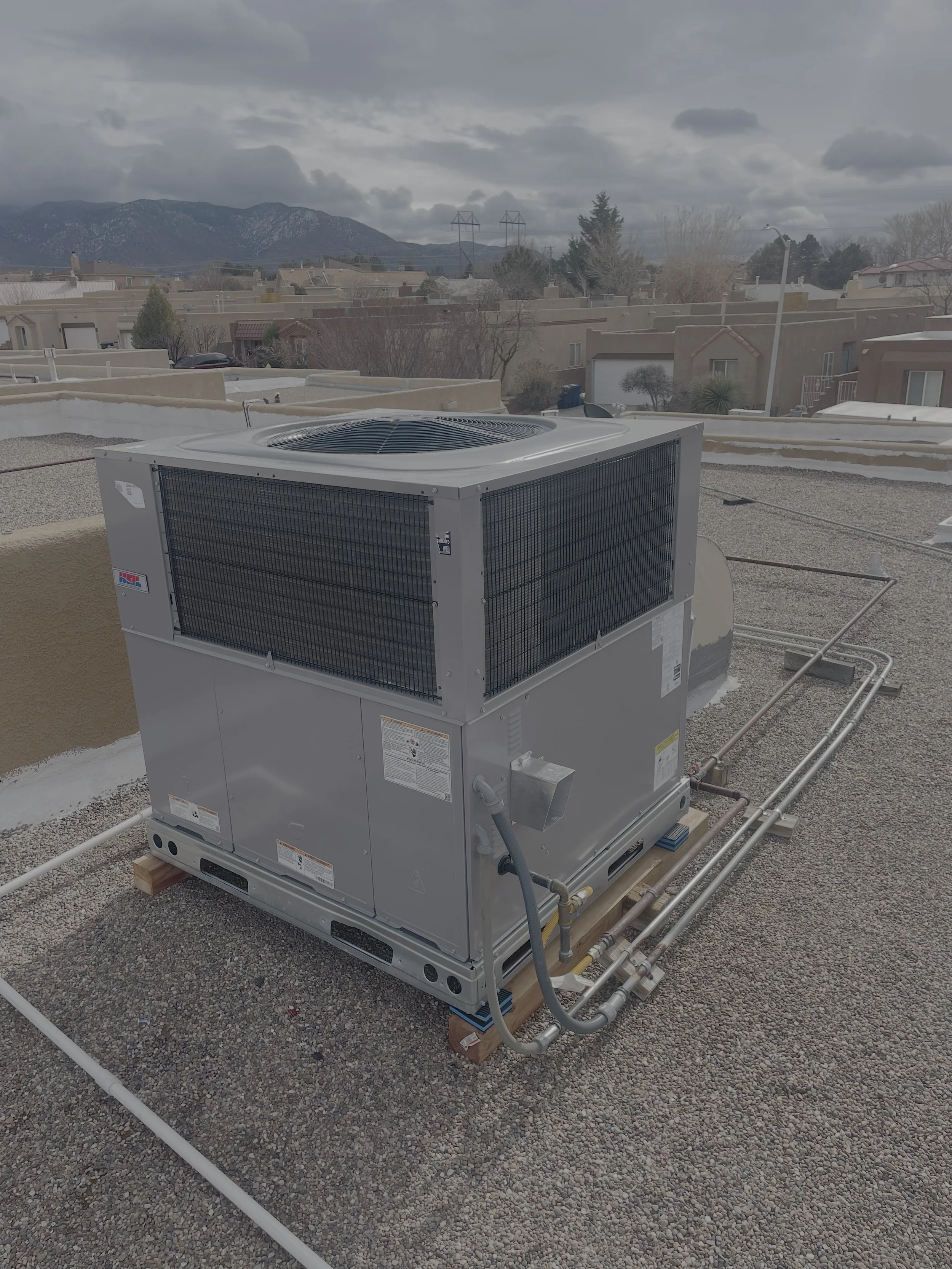 An outdoor HVAC unit on a rooftop with mountains and houses in the background.
