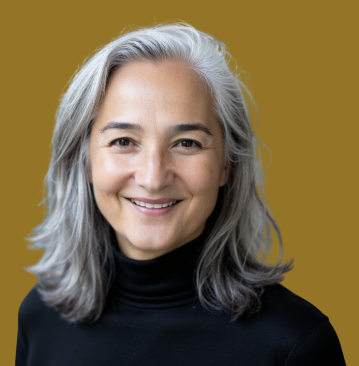 A smiling woman with long gray hair wearing a black turtleneck against a mustard yellow background.