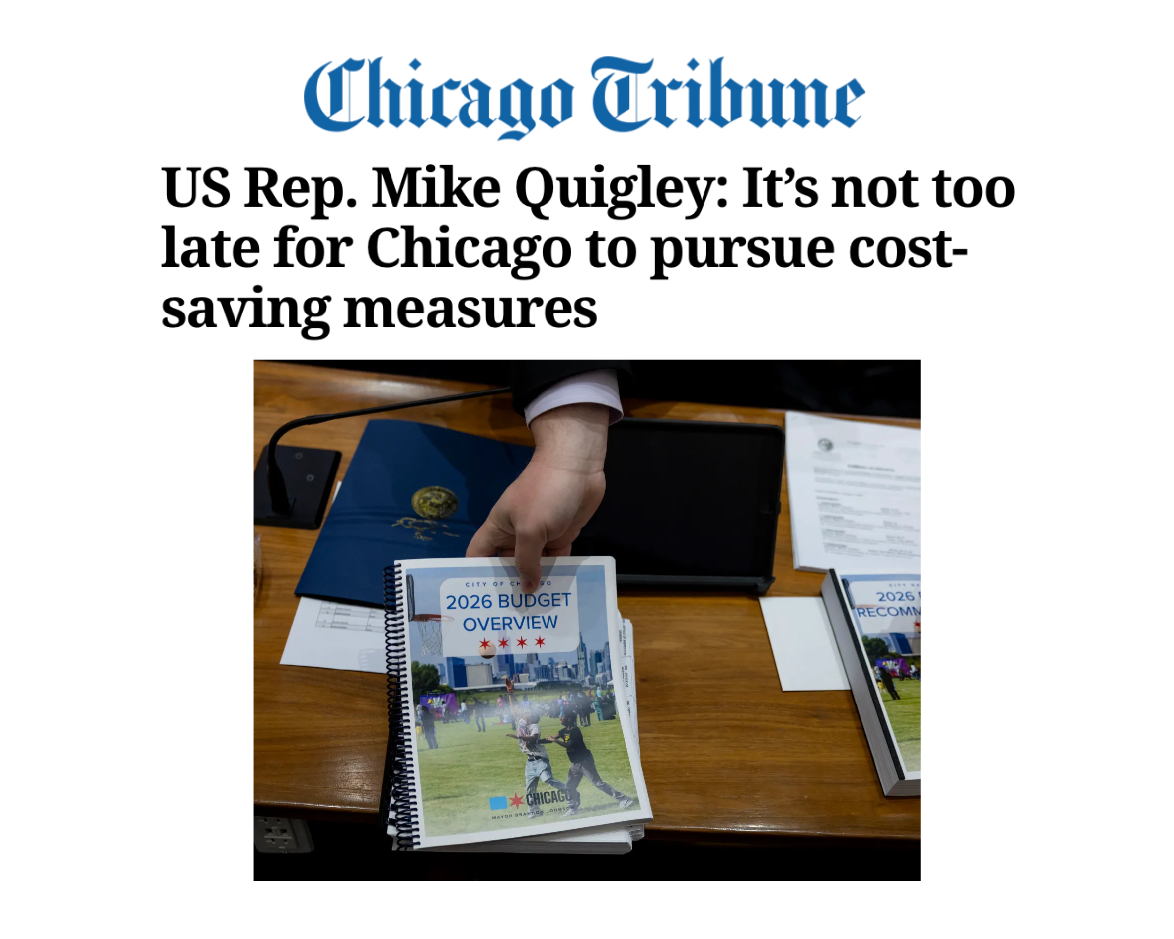 Chicago Tribune headline about US Rep. Mike Quigley's stance on Chicago's budget, featuring a hand pointing at a 2026 budget overview booklet on a desk with documents and a blue folder.