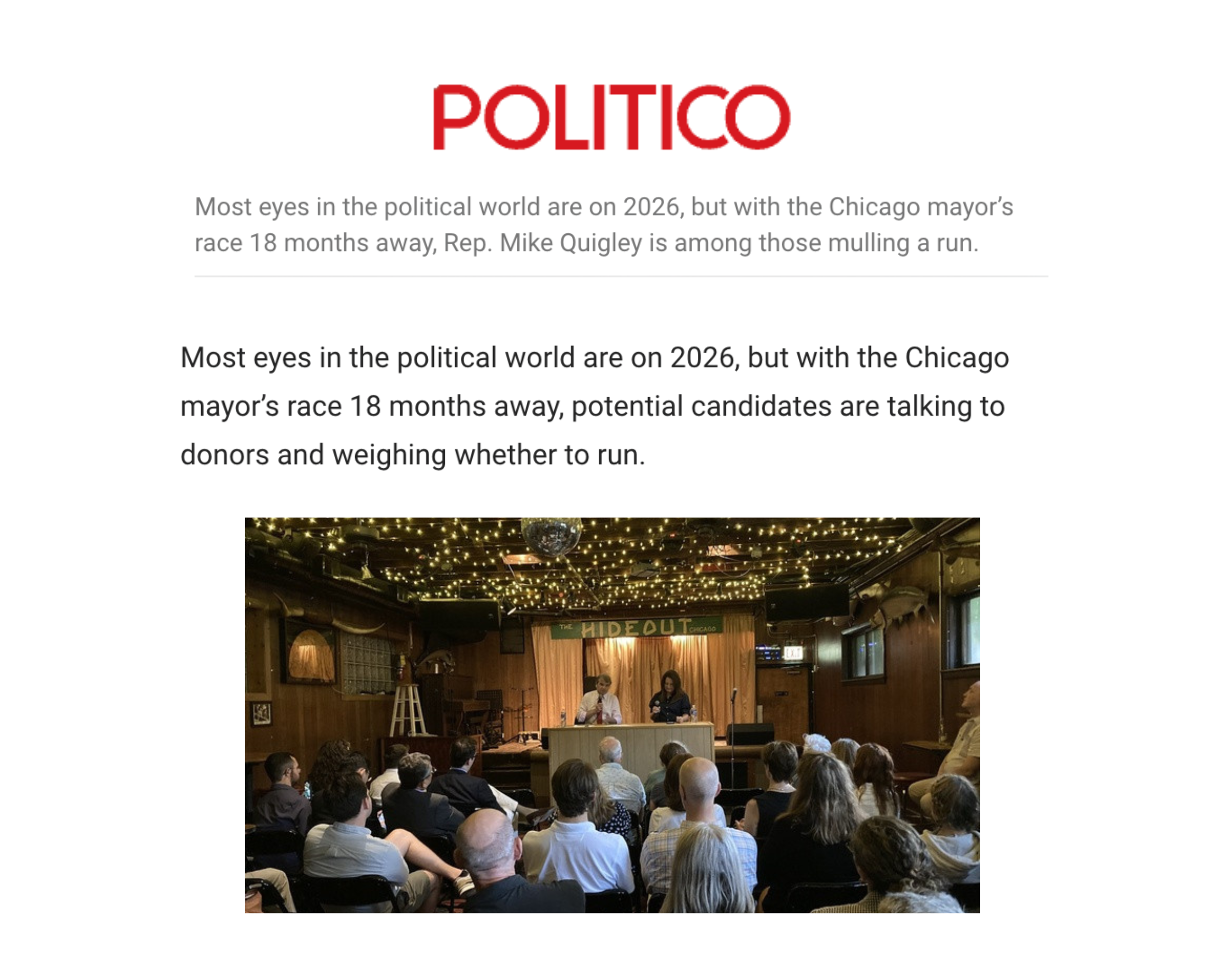 A group of people seated in an indoor venue listening to two speakers on a stage with a sign that reads 'The Hideout'. The ceiling is decorated with string lights and a disco ball.