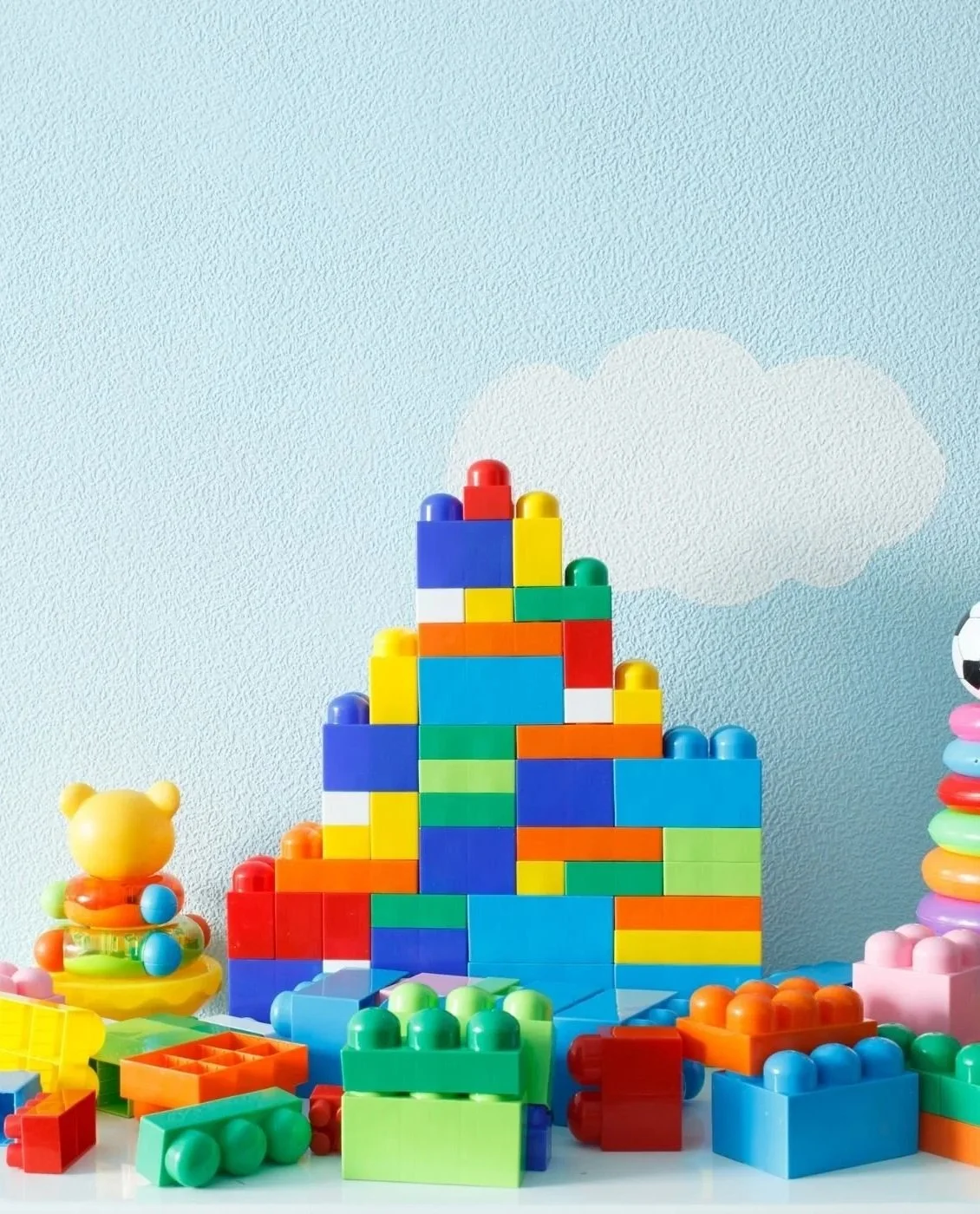 Colorful plastic toy building blocks arranged to resemble a mountain with a cloudy sky background.