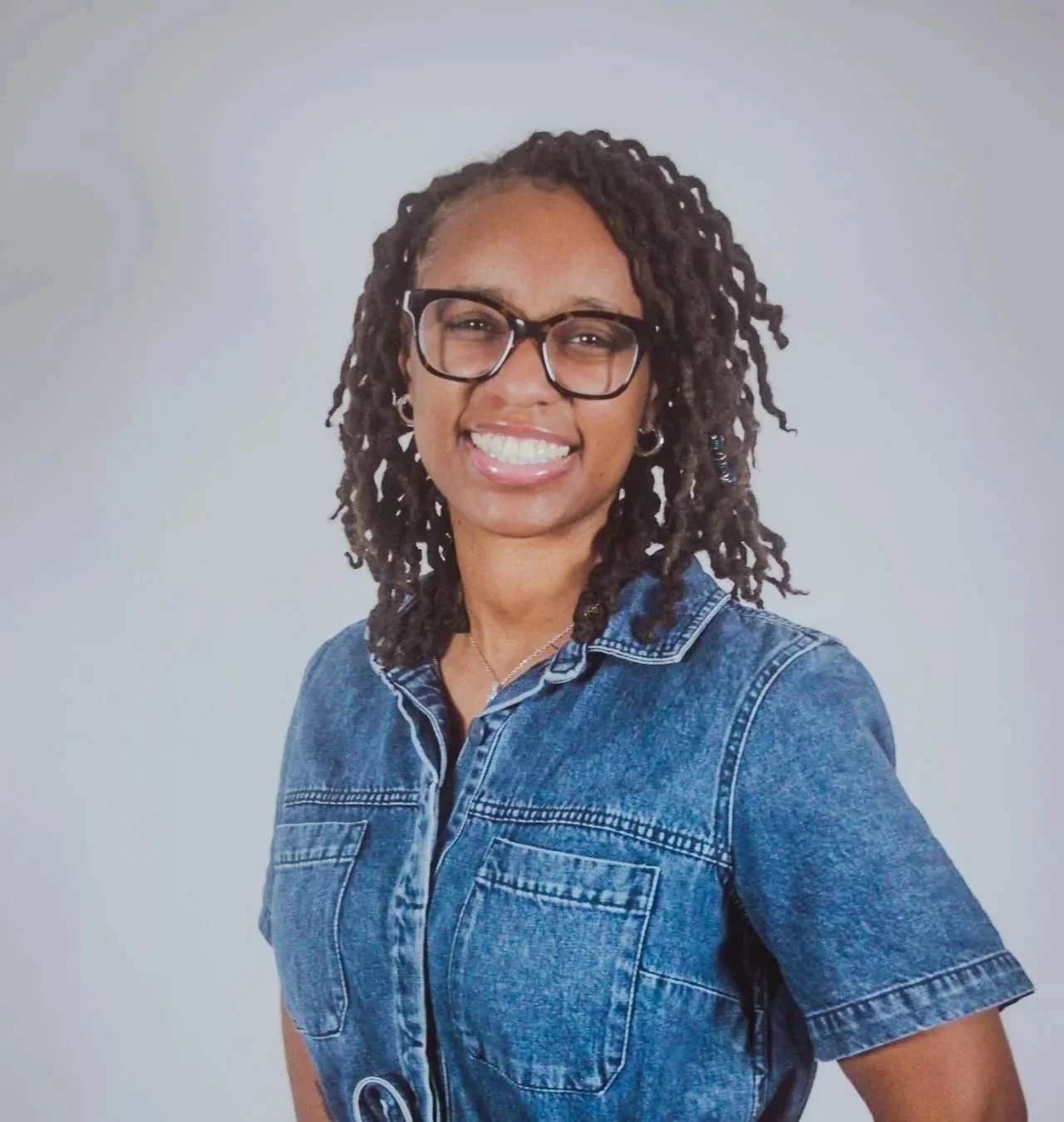 Jacael Wallace, Founder and Owner of Elite Sitters & Care Co, smiling in a denim jacket and silver necklace against a light gray background – experienced childcare professional serving families across DC, Maryland, and Virginia