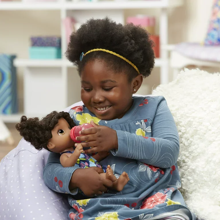 Young girl with curly hair wearing a blue floral dress, sitting on a white fluffy blanket and playing with a doll – symbolizing Elite Sitters & Care Co’s warm, safe, and engaging childcare environment for DMV families.