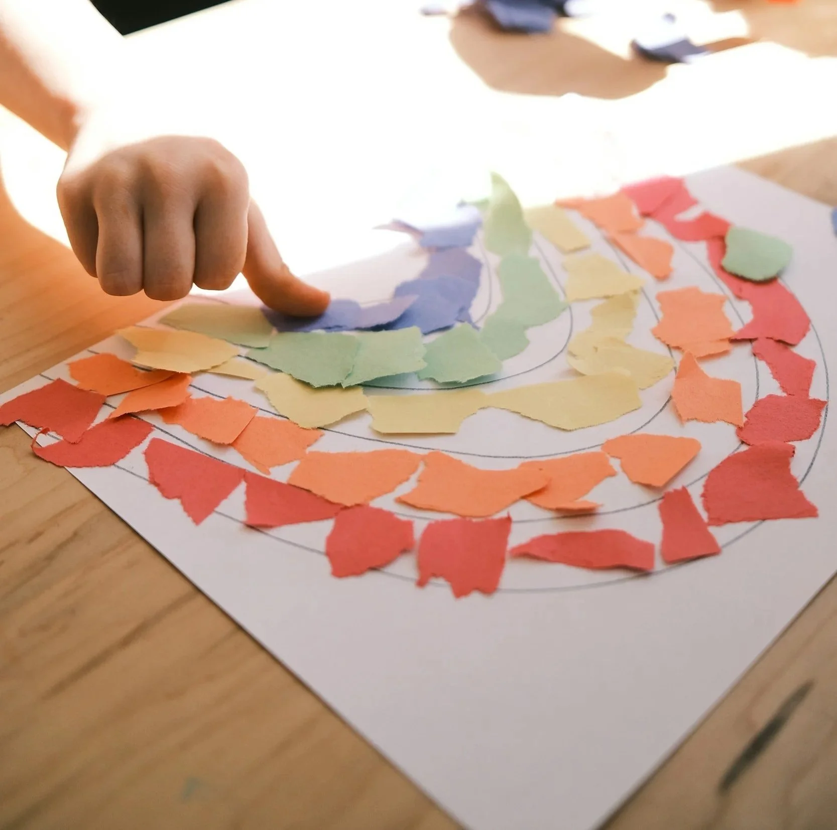 Colorful torn paper pieces arranged on a white paper surface to create a rainbow design.