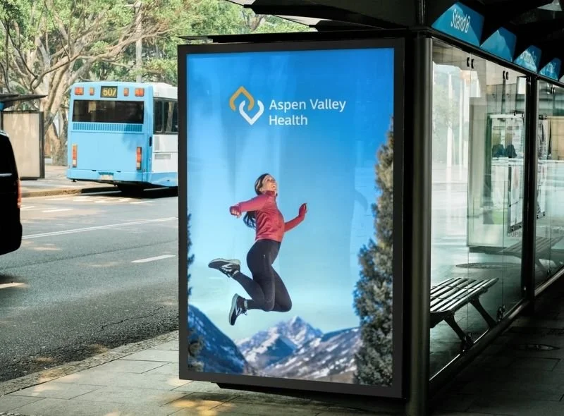 Woman in a red sweater jumping in the air on an Aspen Valley Health advertisement displayed at a bus shelter in Aspen, Colorado