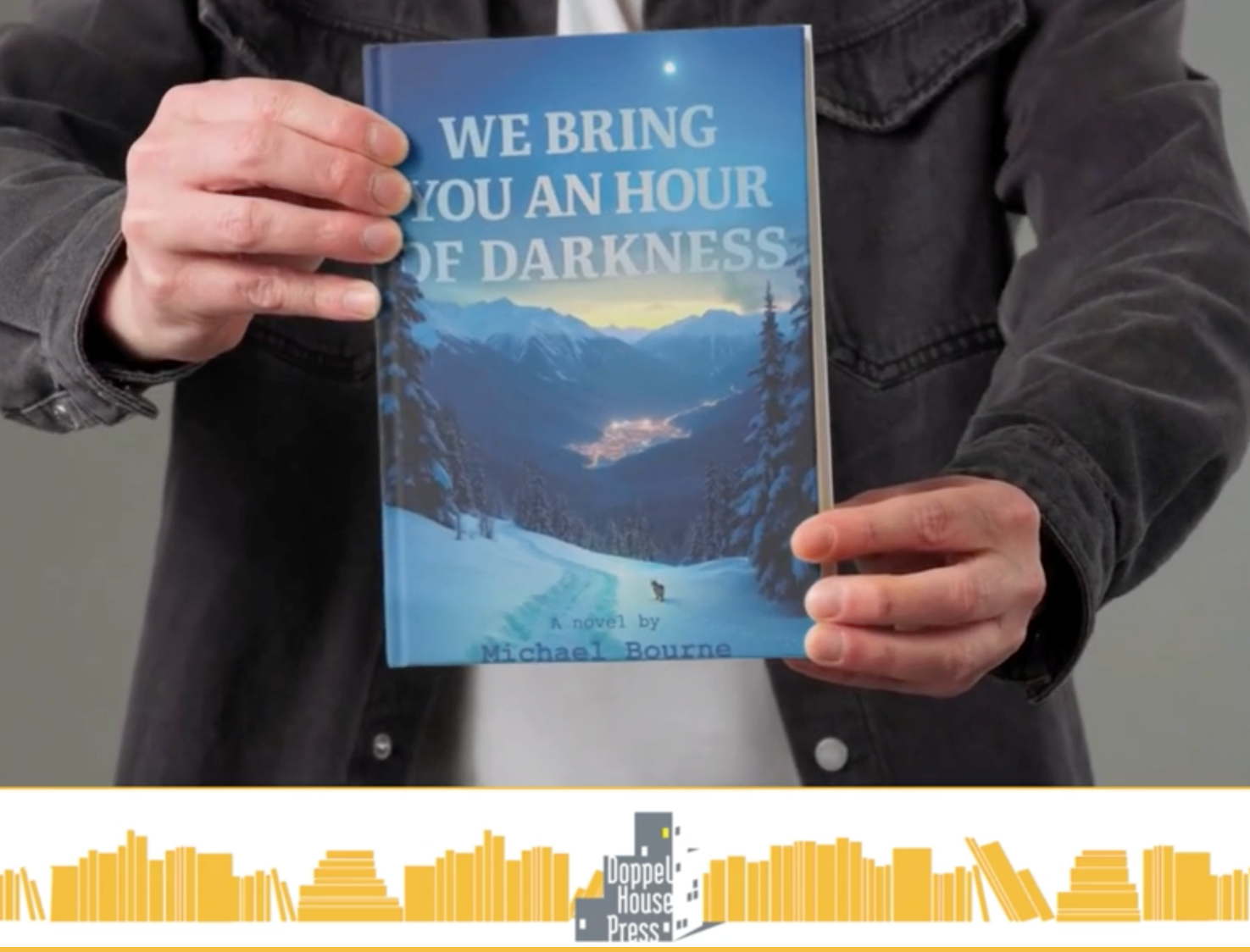 Person holding a book titled "We Bring You an Hour of Darkness" by Michael Bourne, with a scenic mountain landscape with snow and trees on the cover.