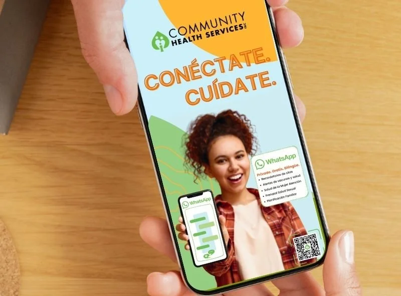 Young woman holding a smartphone displaying a Spanish-language Community Health Services ad with “Conéctate, Cuídate” and WhatsApp branding on bright, colorful graphics