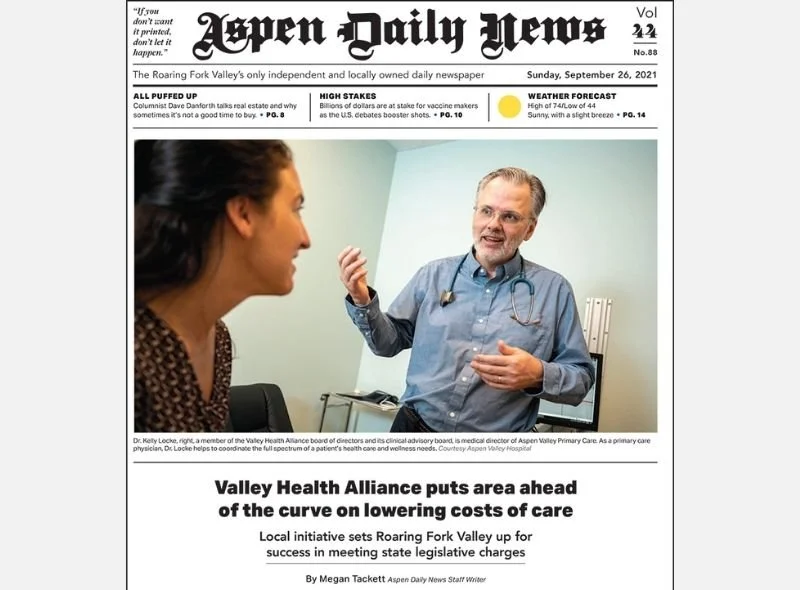 A doctor, Dr. Kelly Locke, speaking to a woman patient in a clinic room, gesturing with his right hand, wearing a stethoscope, with a door and medical equipment in the background.