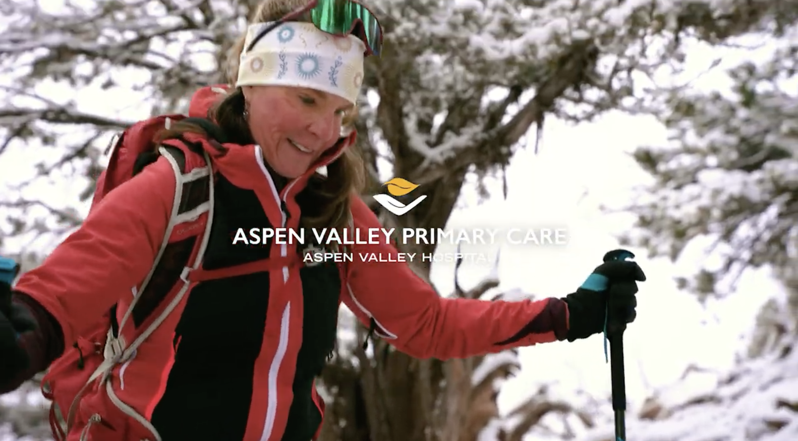 A photo of a mature woman in a red parka cross-country skis in a wintery forest. The Aspen Valley Health logo is superimposed in the middle.