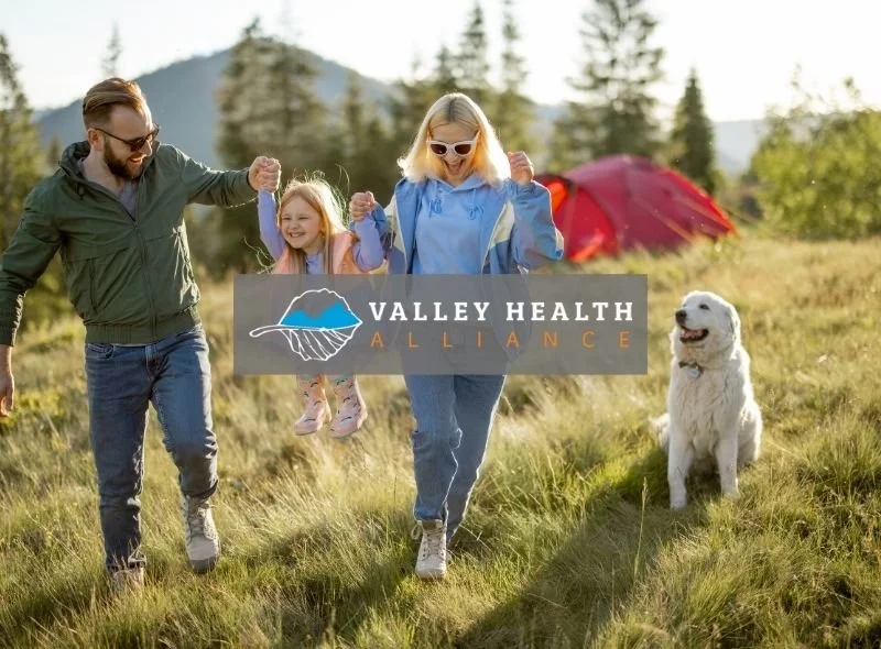 Family with a child and dog running through a mountain landscape with the Valley Health Alliance logo overlaid on the image