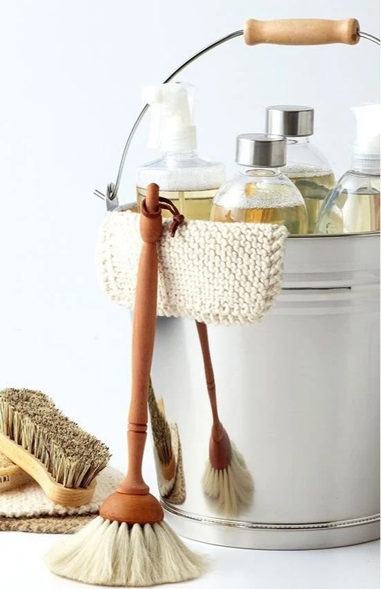 Cleaning supplies including brushes, a knitted pouch, and spray bottles in a metal bucket.