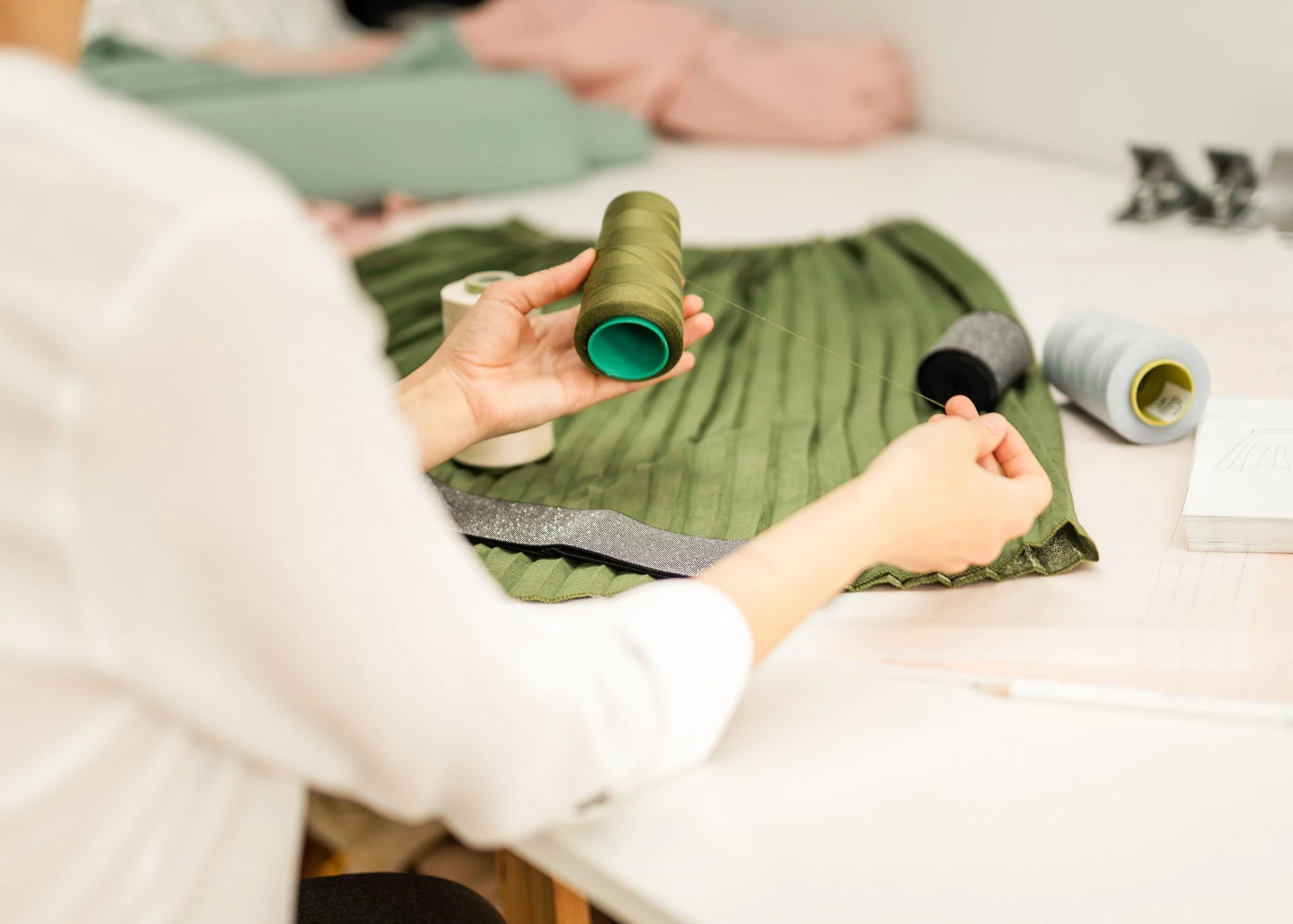 Person sewing green fabric with spools of thread on a table.