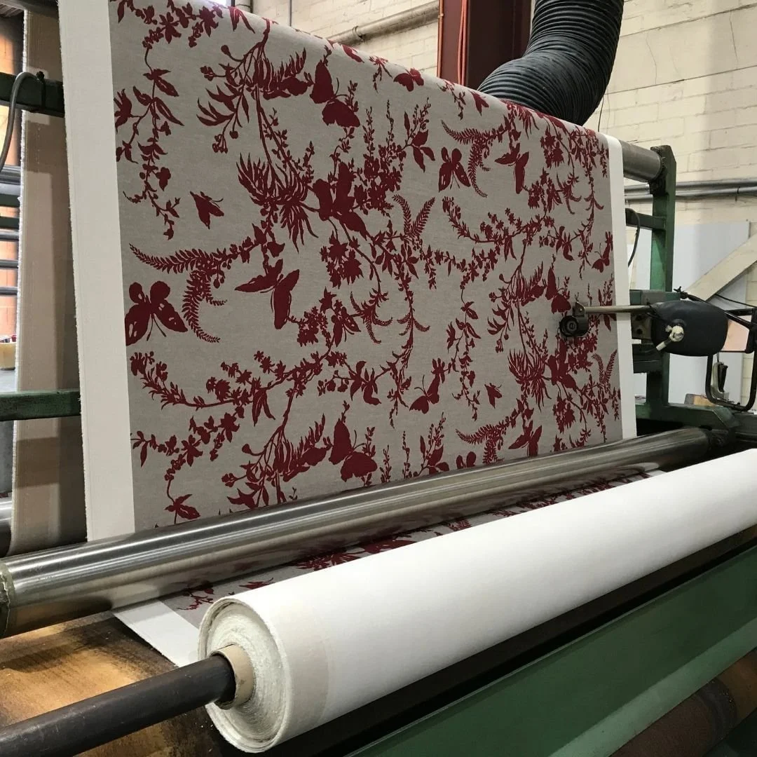 A fabric printing machine printing a fabric with a red and white floral and insect pattern.
