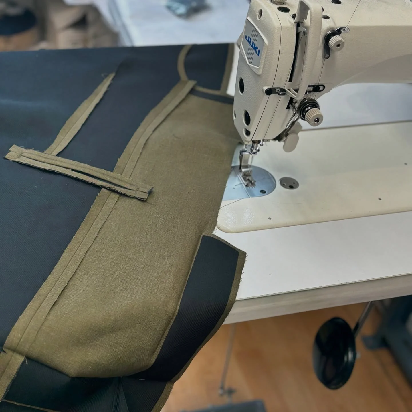 Industrial sewing machine stitching a piece of fabric with a black and olive-green color, on a white table