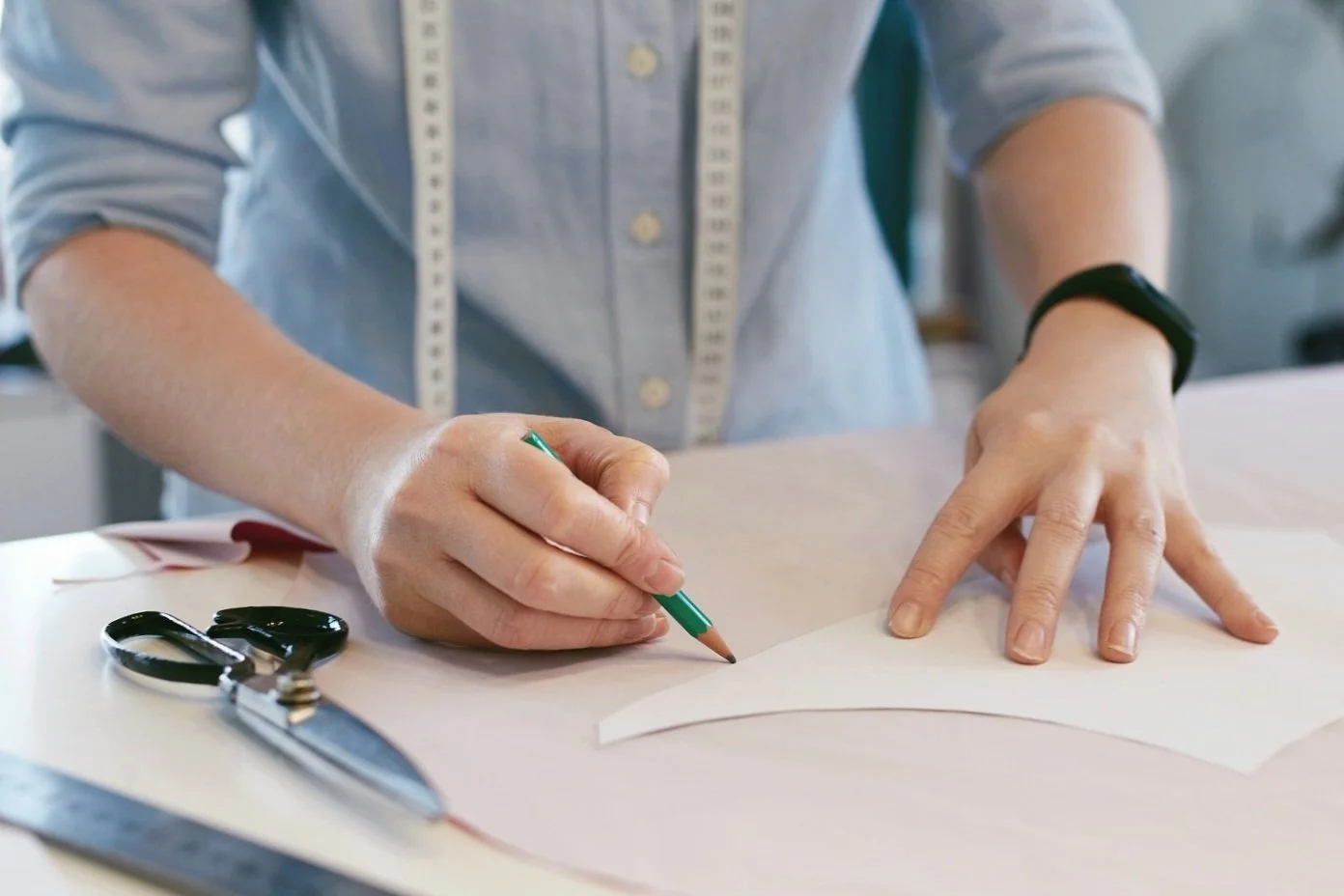 Person working on a sewing or pattern-making project, using a pen to trace on paper with scissors nearby.