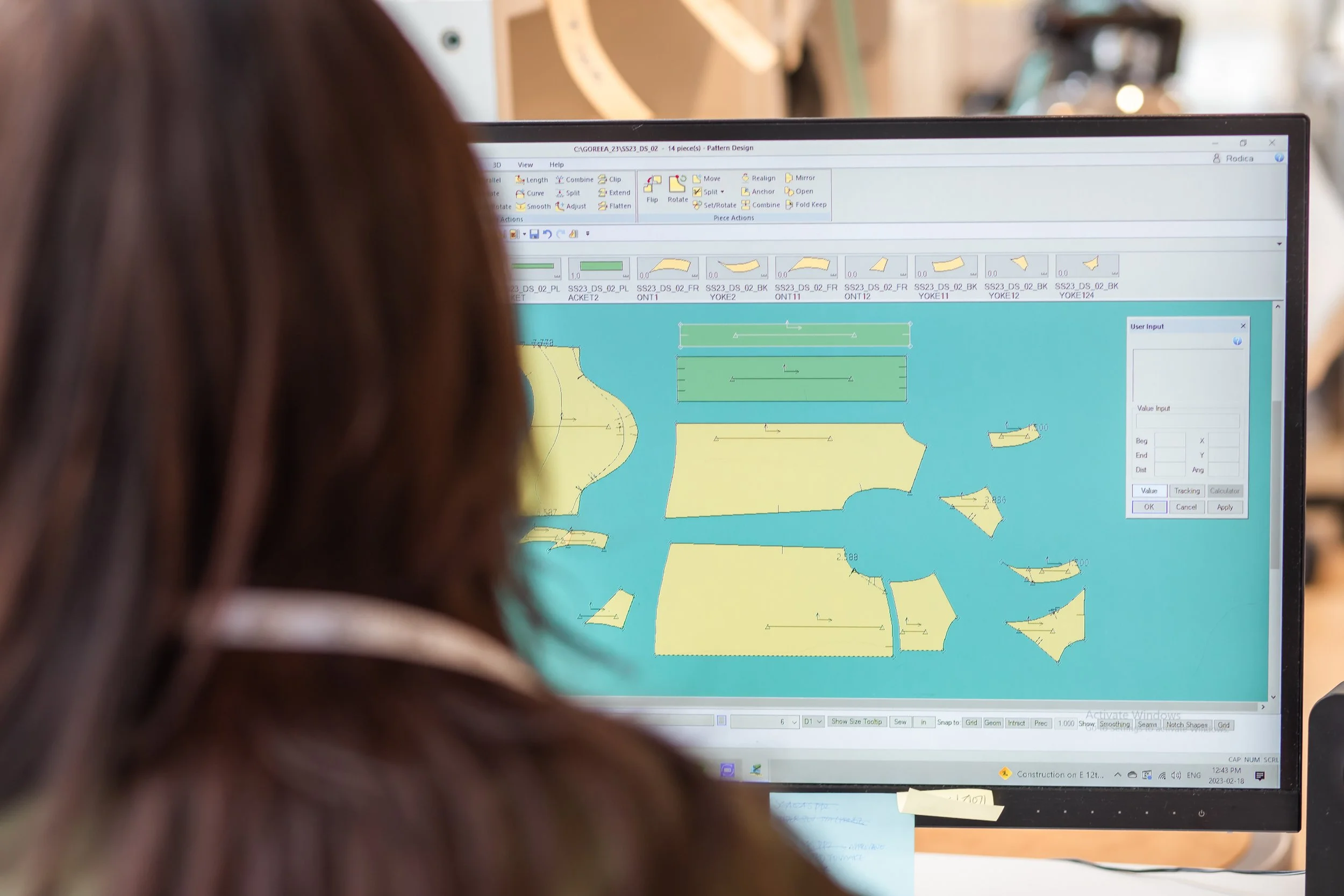 A person with long brown hair working on a computer screen displaying a CAD design for a crafted item, with various patterns and tools visible on the software interface.