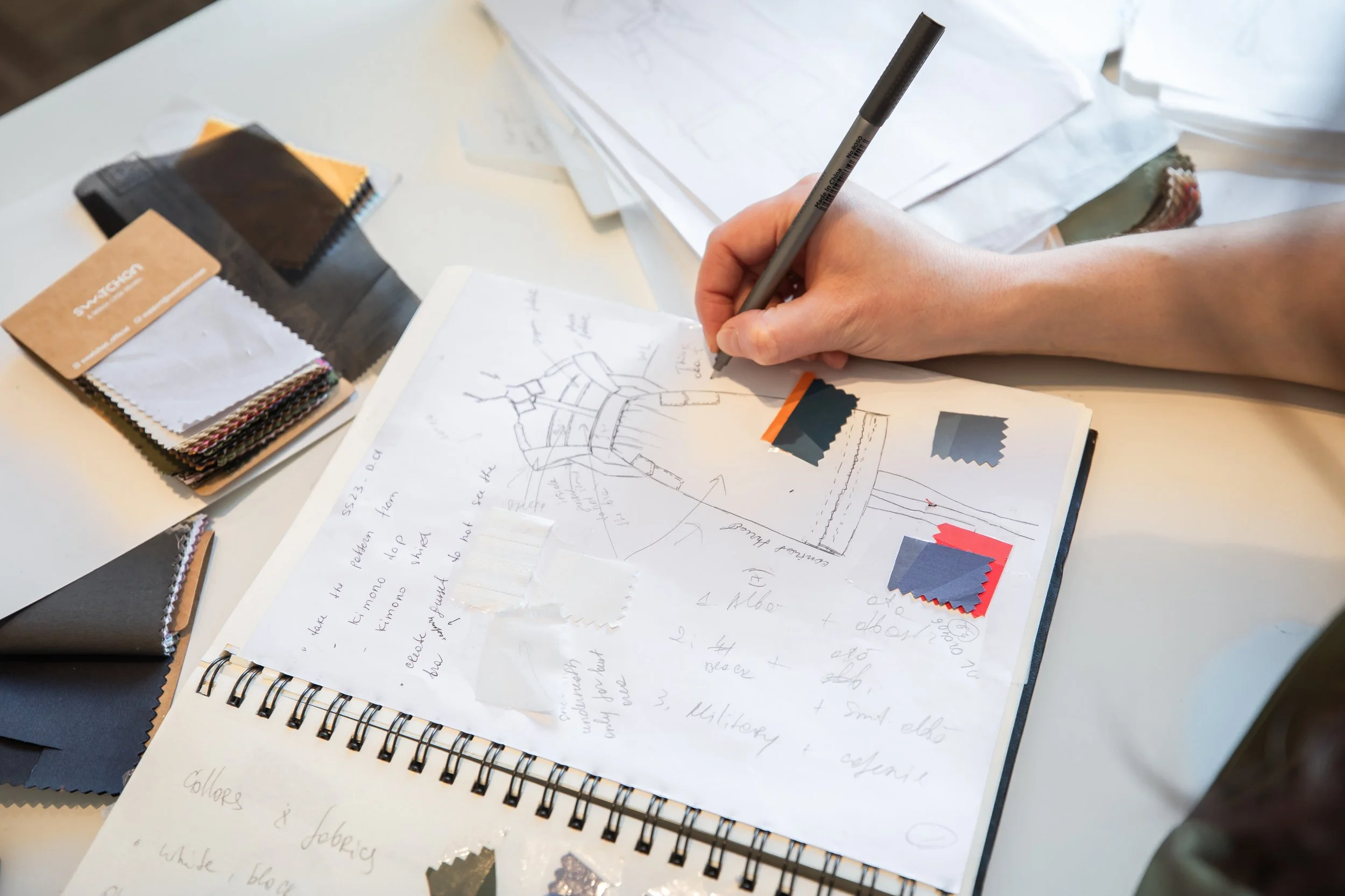Hand drawing a design plan on paper surrounded by fabric samples and notes.