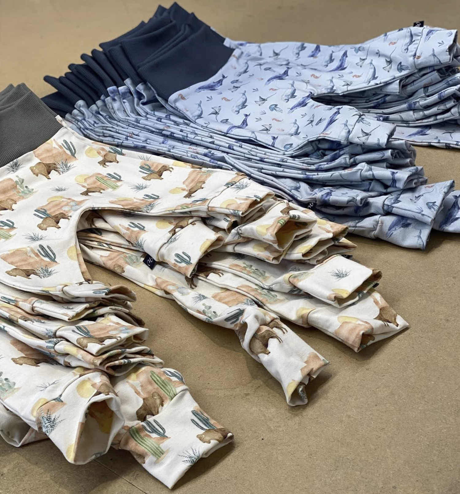 Stacked pajamas with desert animal and plant patterns, arranged on a flat surface.