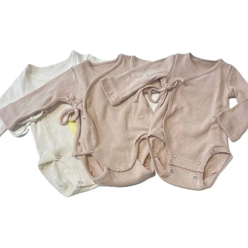 Three baby onesies laid out flat, with long sleeves and snap closures at the bottom, in neutral colors like cream, beige, and light pink.