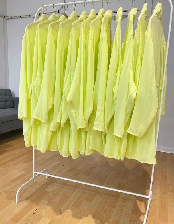 Multiple yellow shirts hanging on a clothing rack inside a room.