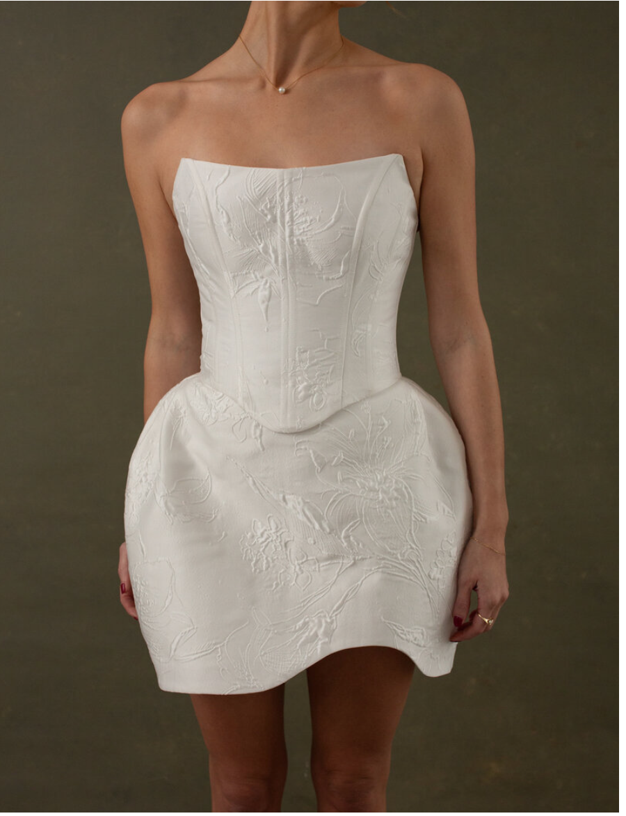 Close-up of woman wearing a strapless white dress with embossed floral patterns and a pearl necklace.