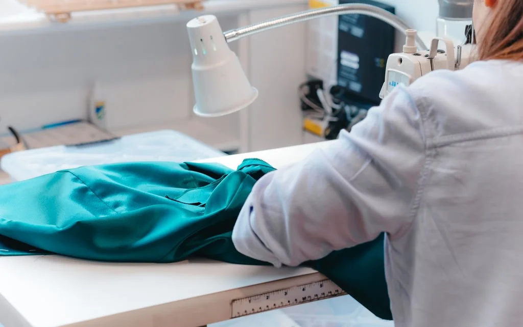 A medical professional in a white coat handling a teal-colored medical garment on a patient’s lap in a clinical setting with medical equipment and monitors in the background.