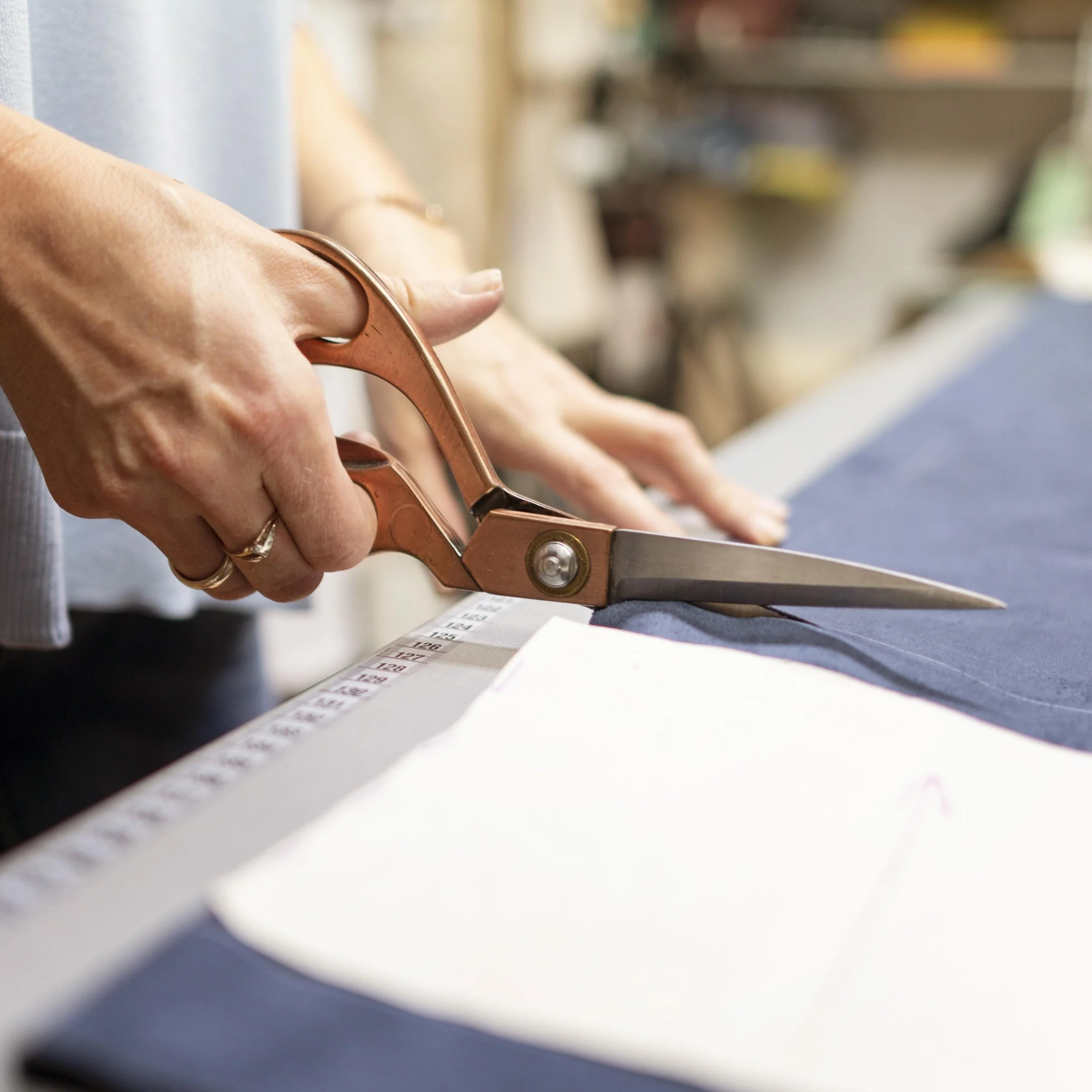 A person cutting fabric with scissors on a sewing table.