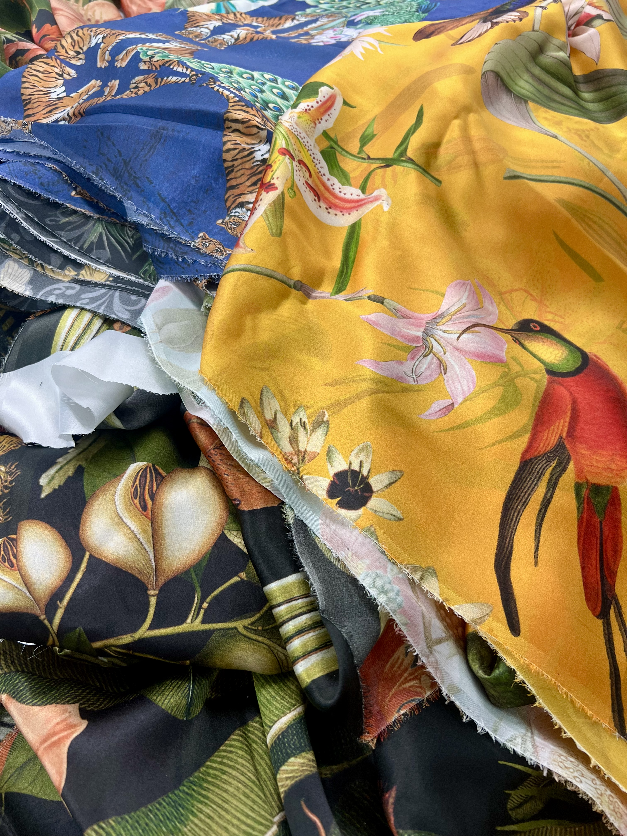 Pile of tropical and wildlife-themed fabric with vibrant colors and detailed animal and plant prints.