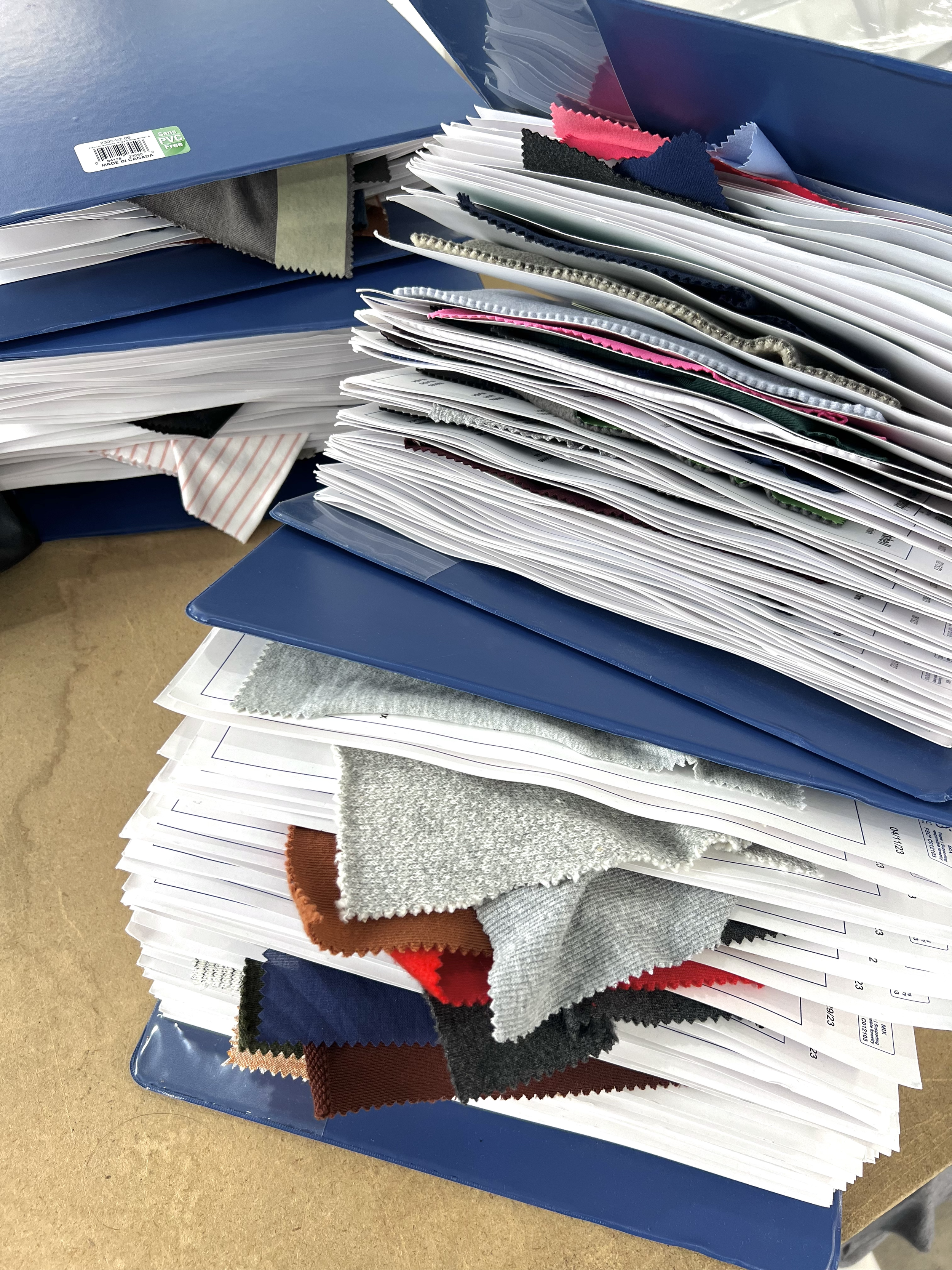 Piles of fabric swatches and paperwork on blue binders.