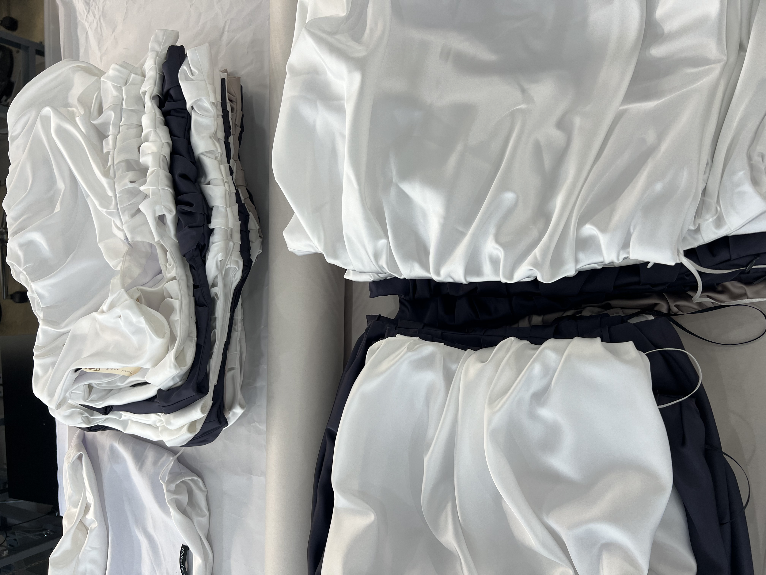 Disorganized pile of white and navy blue satin fabric and clothing items on a white surface, including gathered and ruffled pieces.