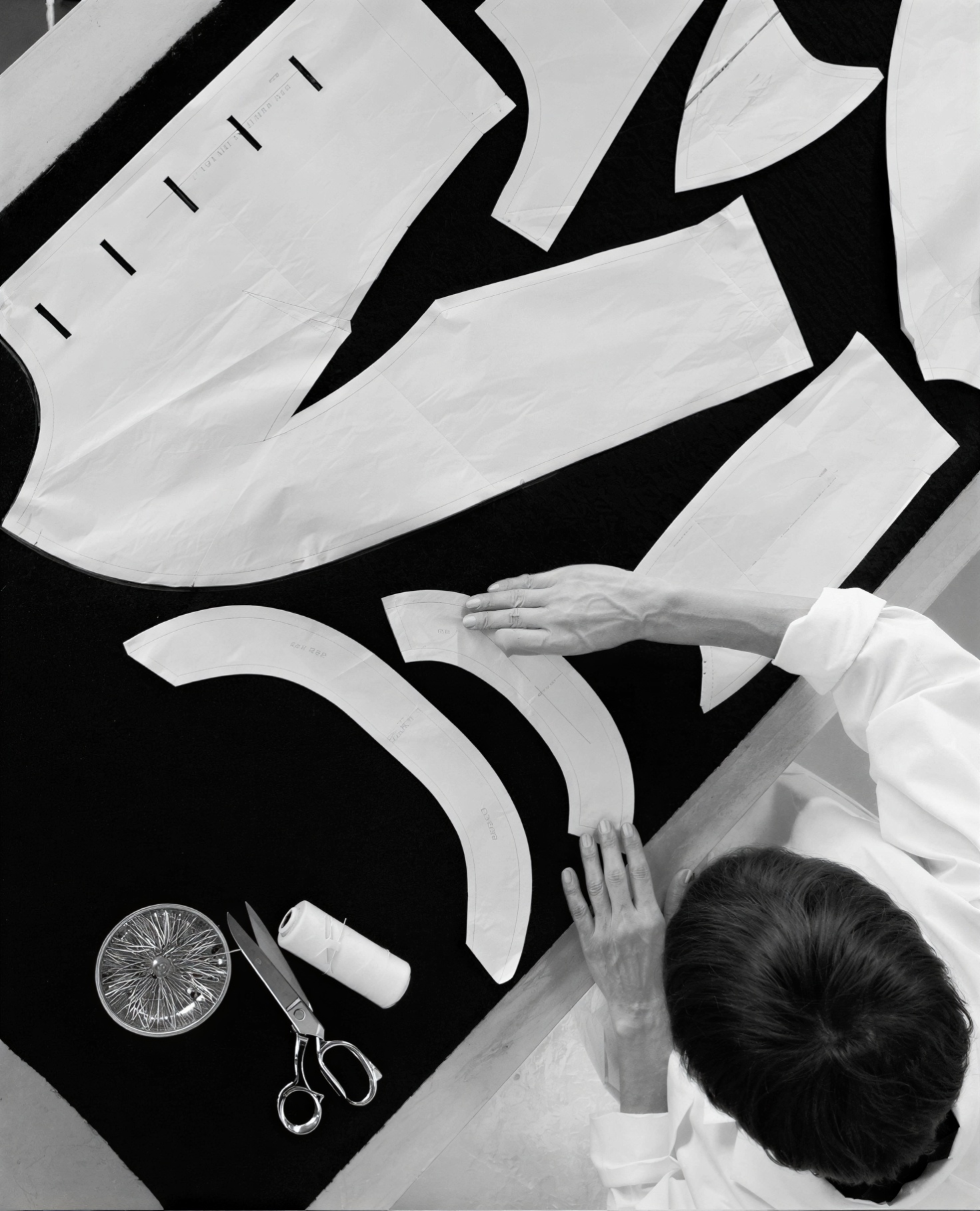 A person sewing fabric pattern pieces on a black worktable, with scissors, thread, and a pin cushion nearby.