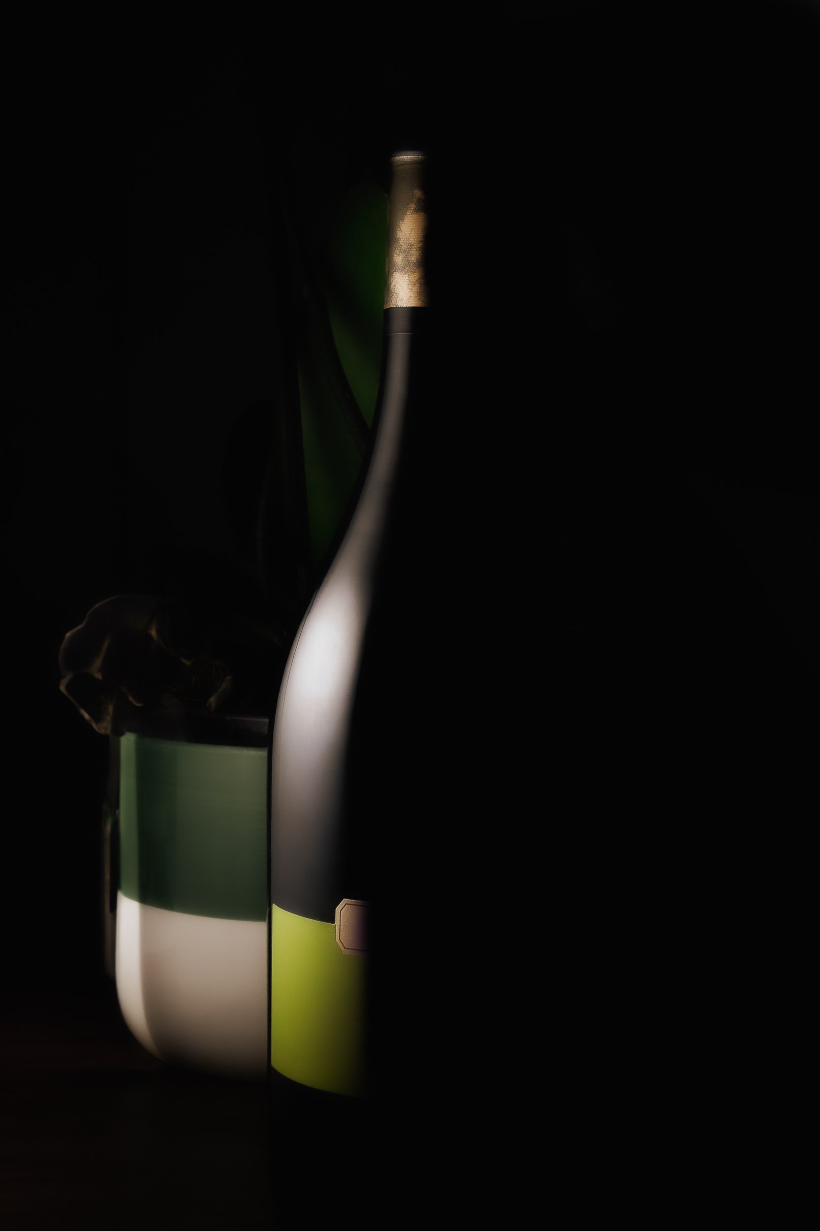 Garrafa e copo de vidro com iluminação suave, escuros ao redor, foco na parte superior da garrafa, fundo escuro.