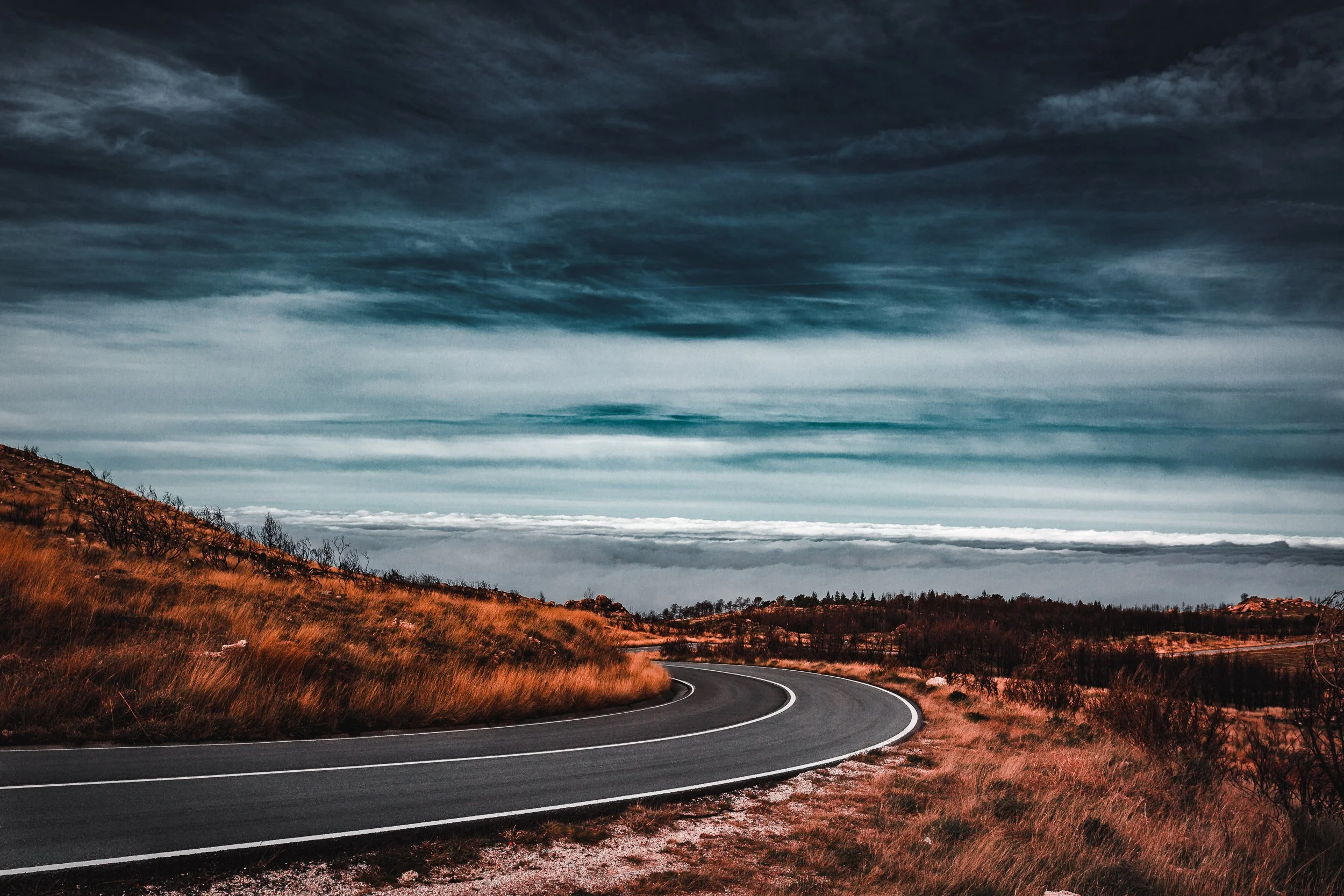 Estrada curvada em um campo de grama dourada sob céu carregado de nuvens escuras