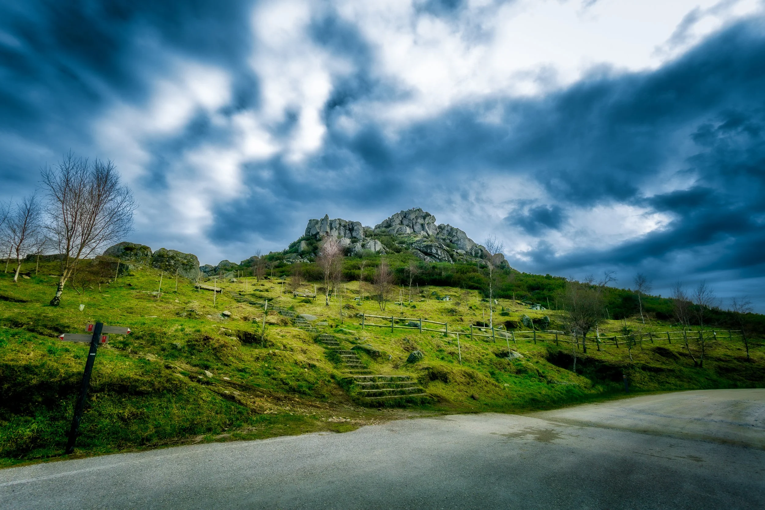 Paisagem de montanha com céu nublado, árvores e escadas de pedra na encosta.