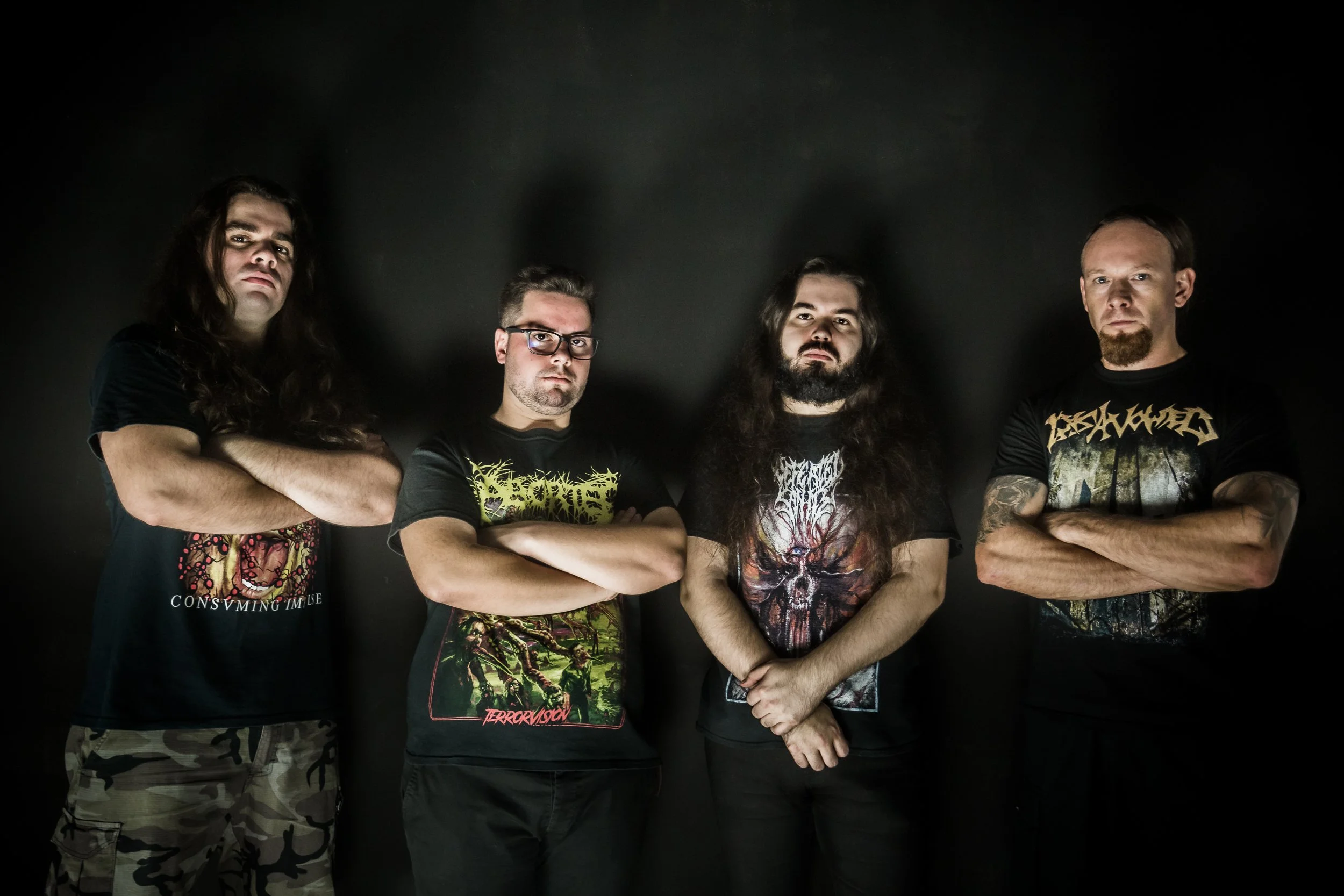 Quatro homens com roupas de banda de metal, com braços cruzados, posando contra fundo preto.
