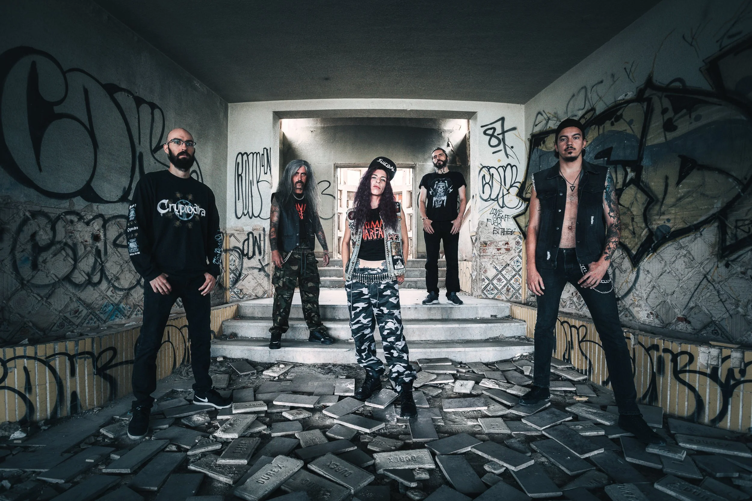 Cinco pessoas posando em uma passagem subterrânea com paredes grafitadas, com uma delas no centro usando roupa de rocinha