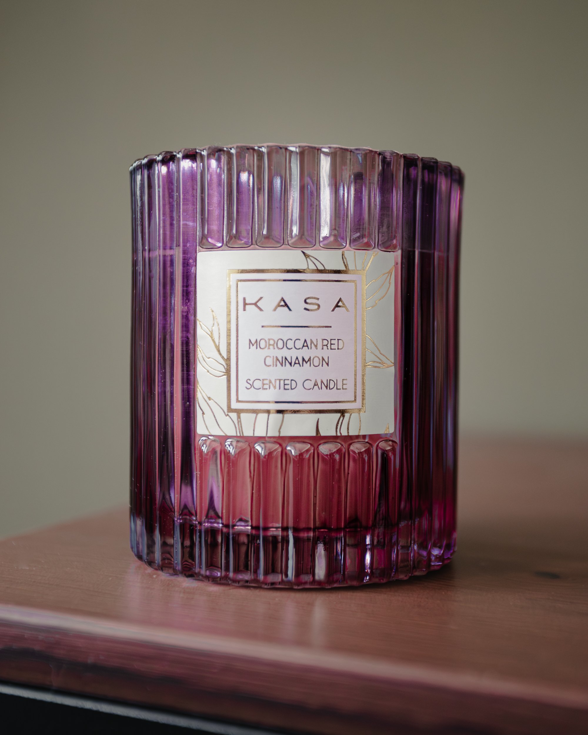 Vela decorativa de vidro rosa com ranhuras verticais, etiqueta branca com detalhes dourados, texto em português e inglês indicando "KASA Vela Aromática de Canela Vermelha Marroquina"
