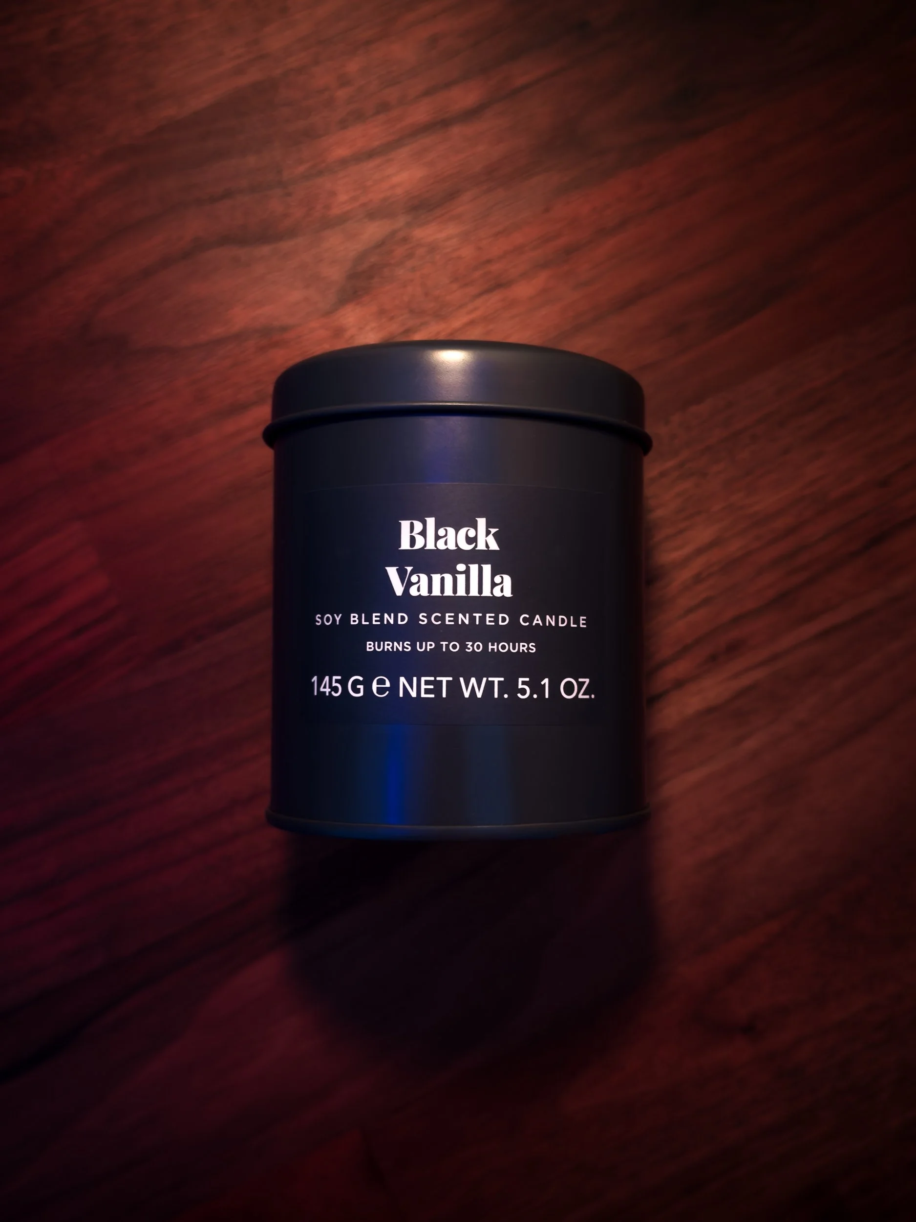 Vela aromática com embalagem preta e etiqueta escrita em inglês, indicando 'Black Vanilla', feita de uma mistura de soja, com duração de queima de até 30 horas, peso de 145 gramas ou 5.1 onças.