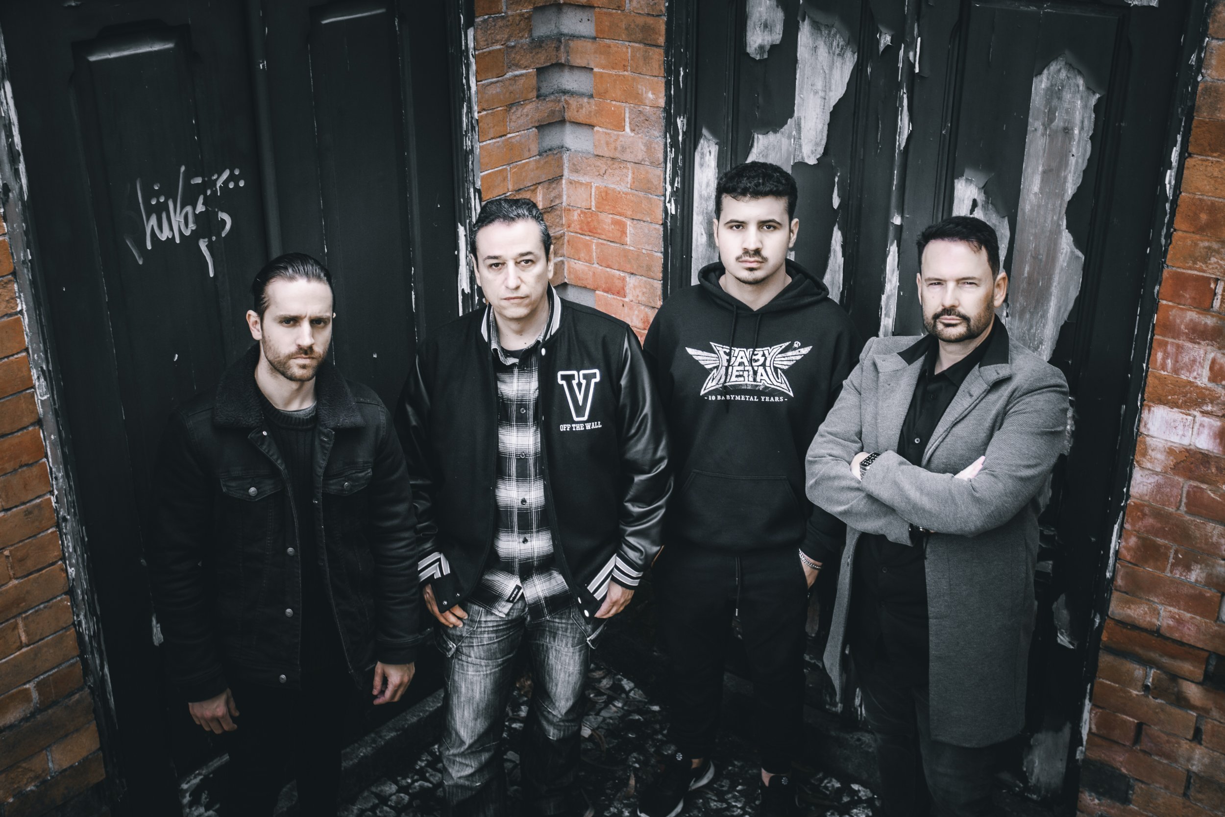 Quatro homens em uma parede de fundo de tijolos e portas de madeira preta