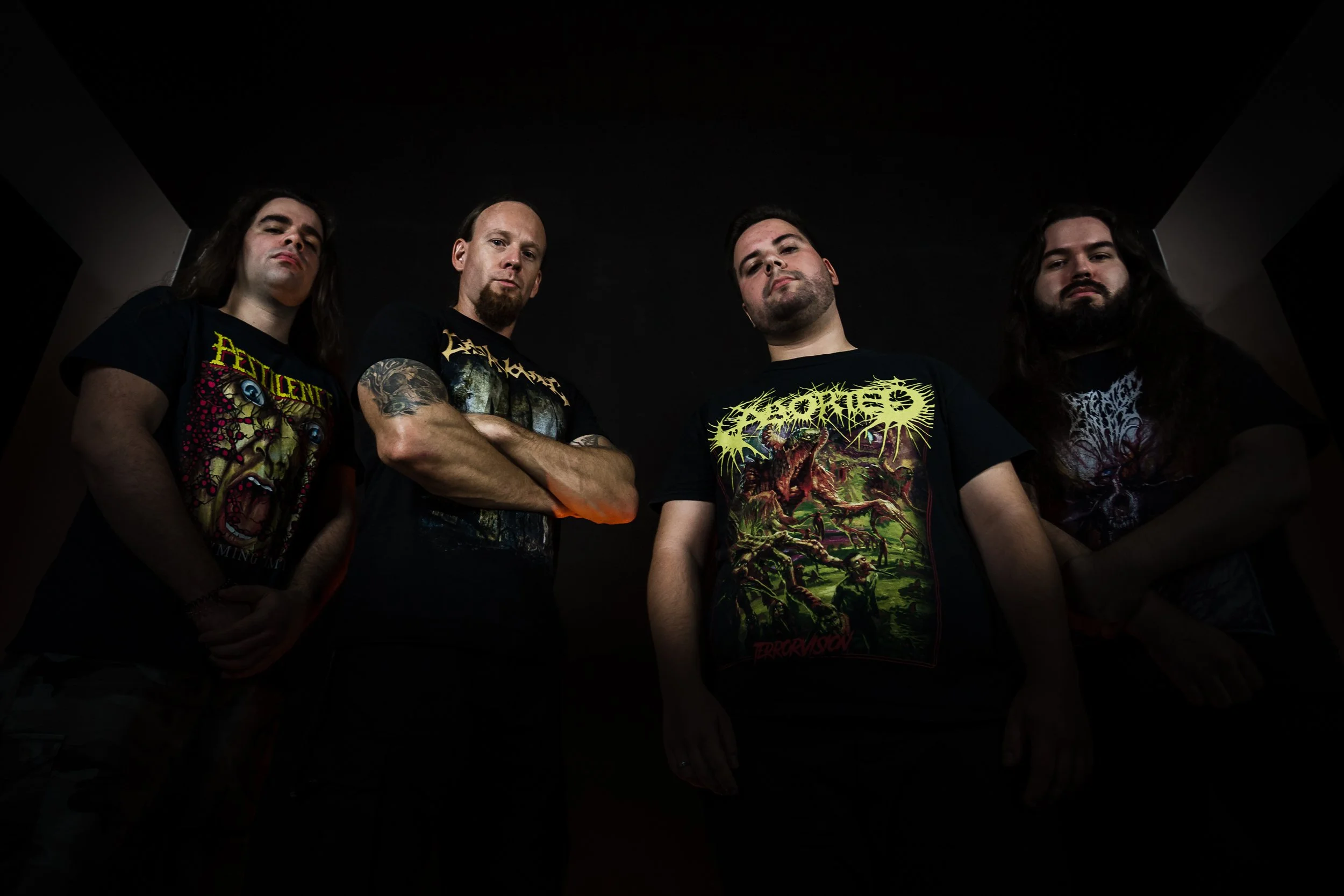 quatro homens com roupas de banda de heavy metal posando em um ambiente com iluminação escura