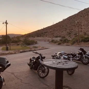 Motorcycles parked on a dirt lot near a mountain at sunset.
