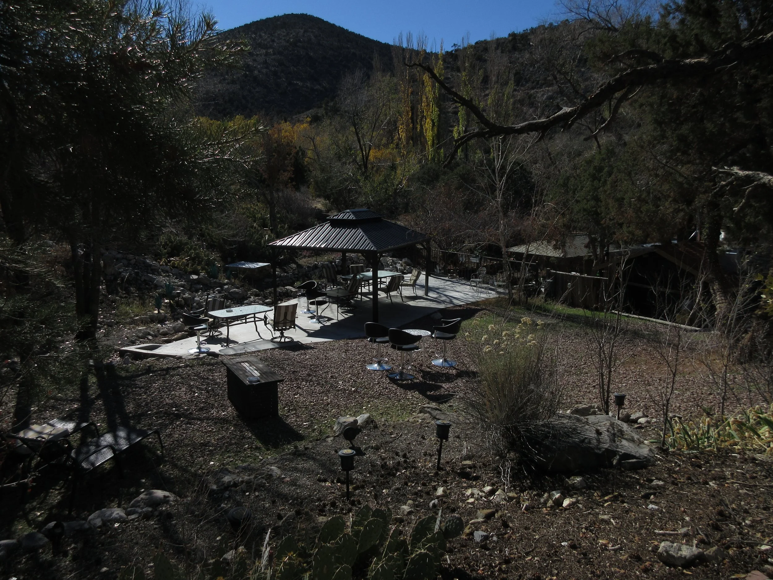 Outdoor patio with tables, chairs, and a shaded umbrella in a mountainous wooded area.