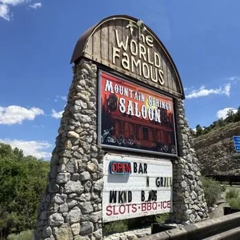 Sign for the World Famous Mountain Springs Saloon, showing it is an open bar and grill with slots, BBQ, and ice.