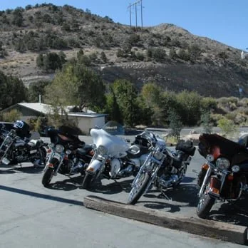 Several motorcycles parked on a lot with a mountain and trees in the background.