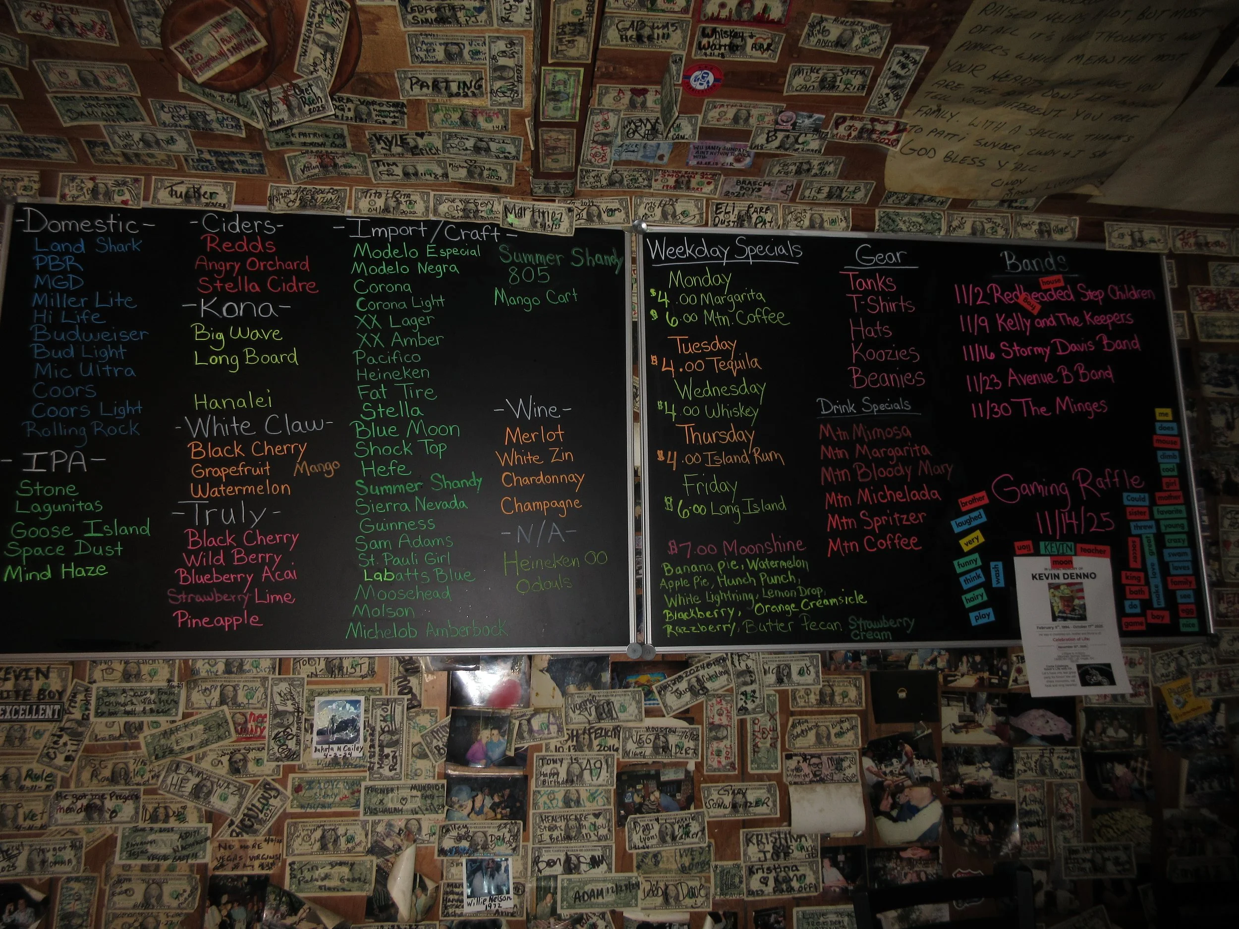 A wall display with two blackboards listing craft beer and drink specials, surrounded by dollar bills and photographs on a brick wall.