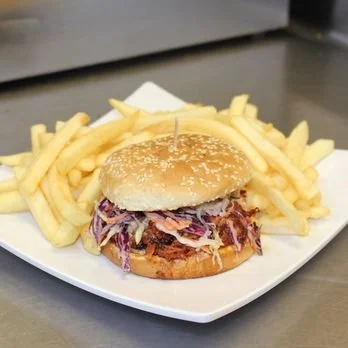 A chicken sandwich with coleslaw on a bun, served with French fries on a white plate.