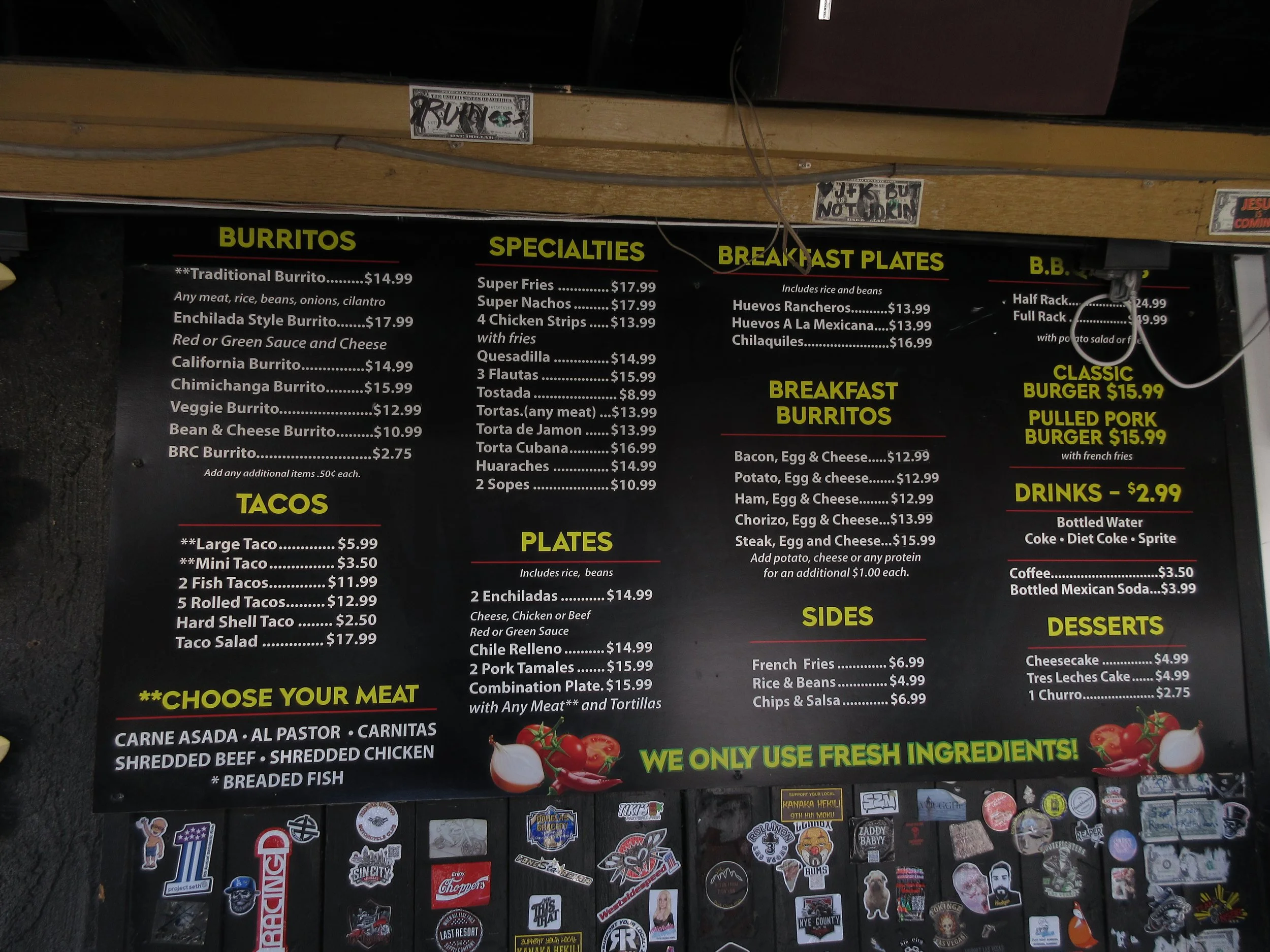 Menu board with burritos, tacos, specialities, breakfast plates, sides, drinks, and desserts at a Mexican restaurant, featuring prices and options.