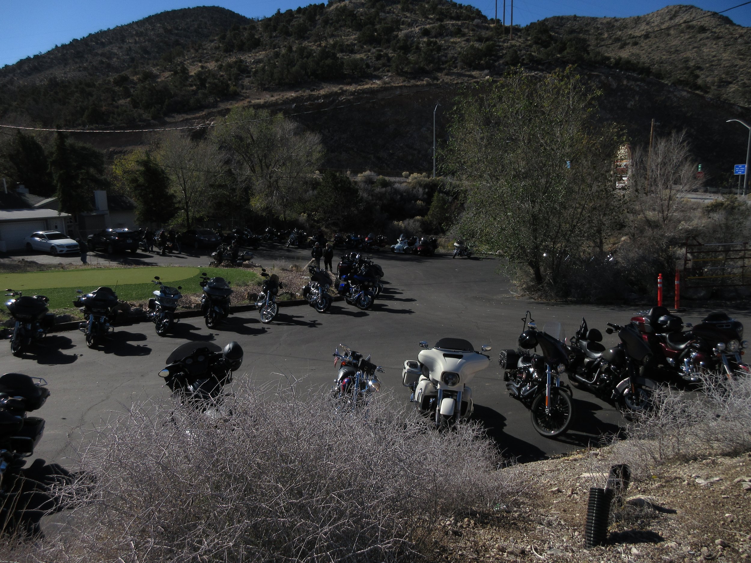 A parking lot filled with motorcycles and a few cars, with hills and trees in the background.